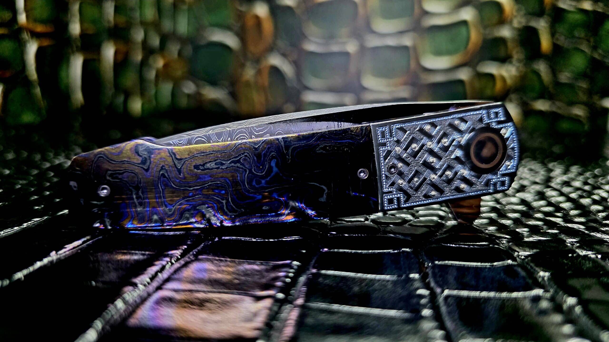 Herucus Blomerus custom folding knife open on dark surface showing carbon fiber handle and satin drop point blade