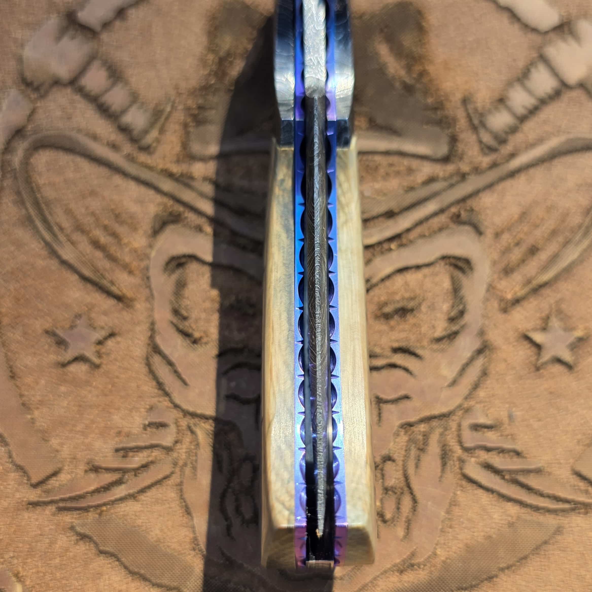 Looking directly down the spine of the closed Scott Gallagher Sukattuk Flipper, showing the Mosaic Damascus blade perfectly centered between the engraved titanium liners and natural mammoth ivory scales.