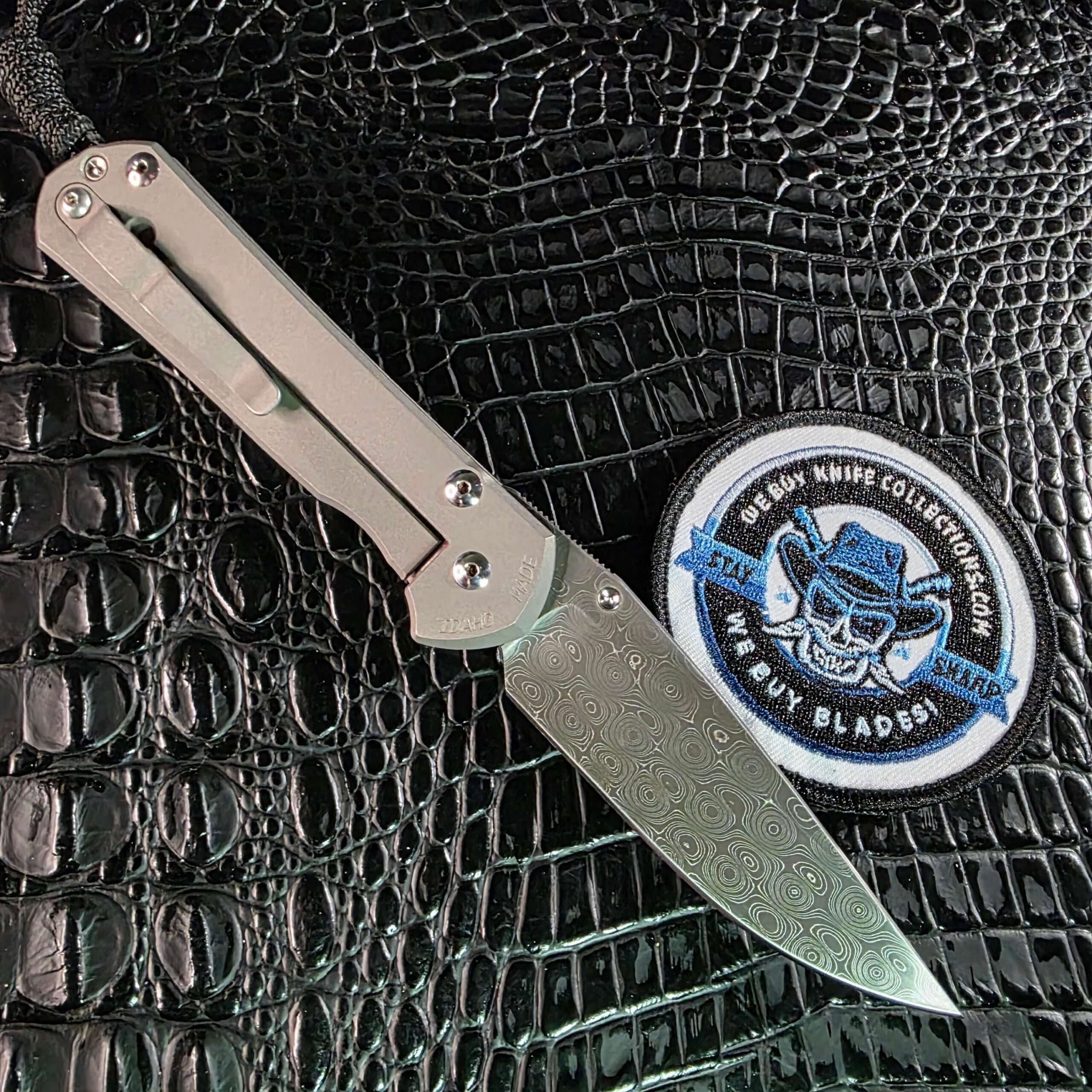 Chris Reeve Sebenza 21 Damascus blade open beside We Buy Knife Collections patch