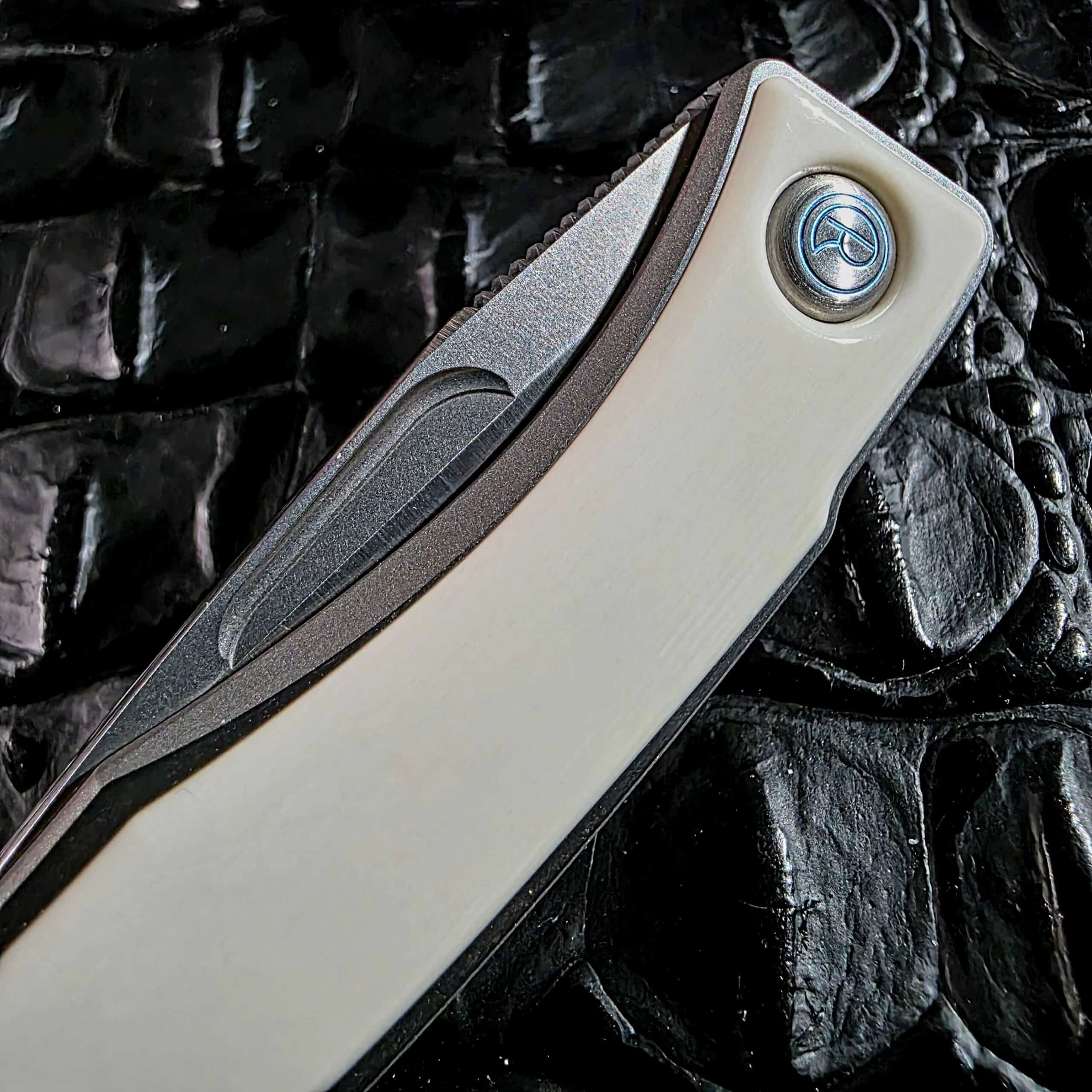 Macro of the blue-anodized Chris Reeve logo pivot medallion set into white mammoth ivory on the Mnandi