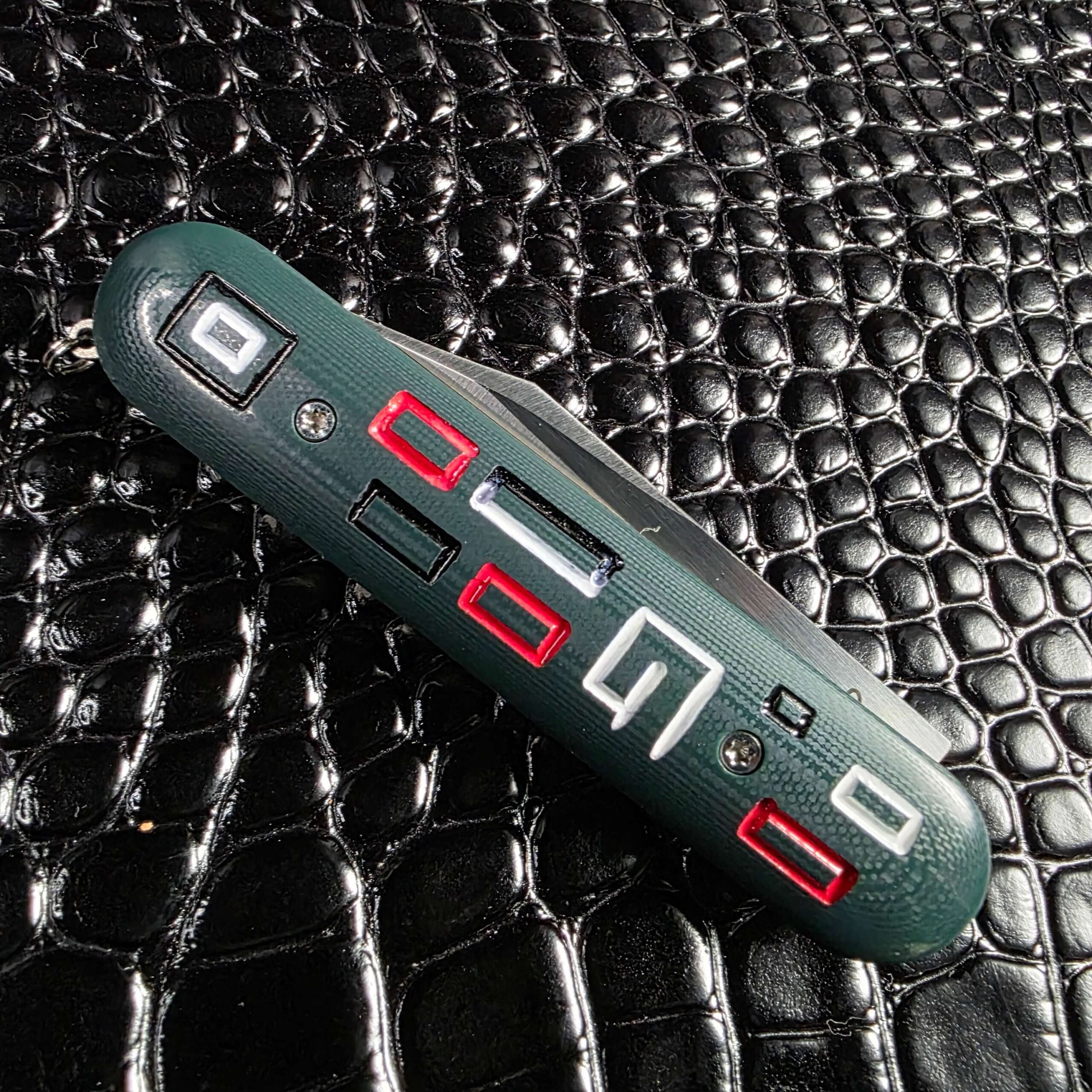 Macro of the milled green G-10 mosaic and the maker's G logo on the Chuck Gedraitis Switch Army Switchblade