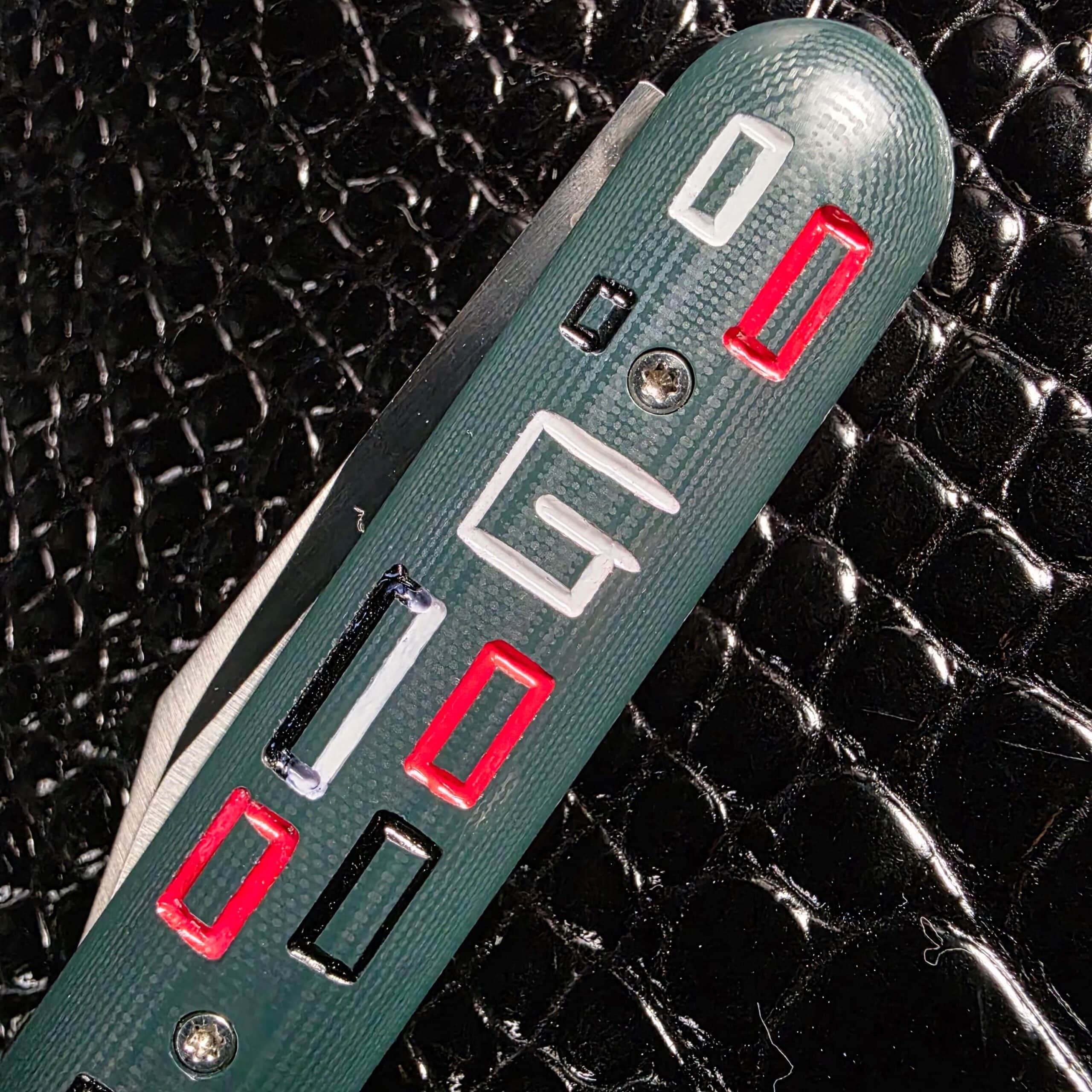 Macro of the milled green G-10 mosaic and the maker's G logo on the Chuck Gedraitis Switch Army Switchblade