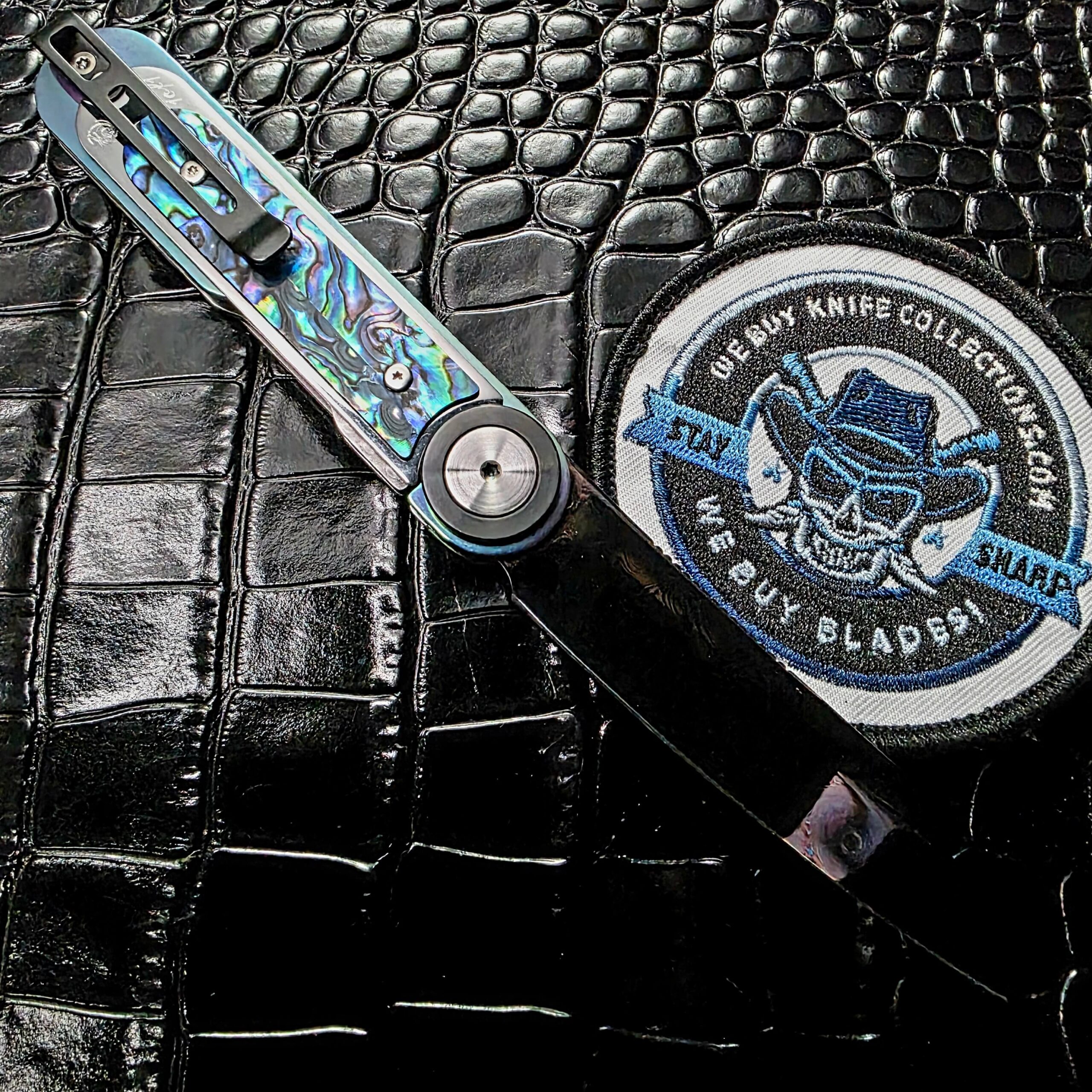 Dew Hara Infinity open on the clip side beside the We Buy Knife Collections patch, 1of1 engraved pocket clip