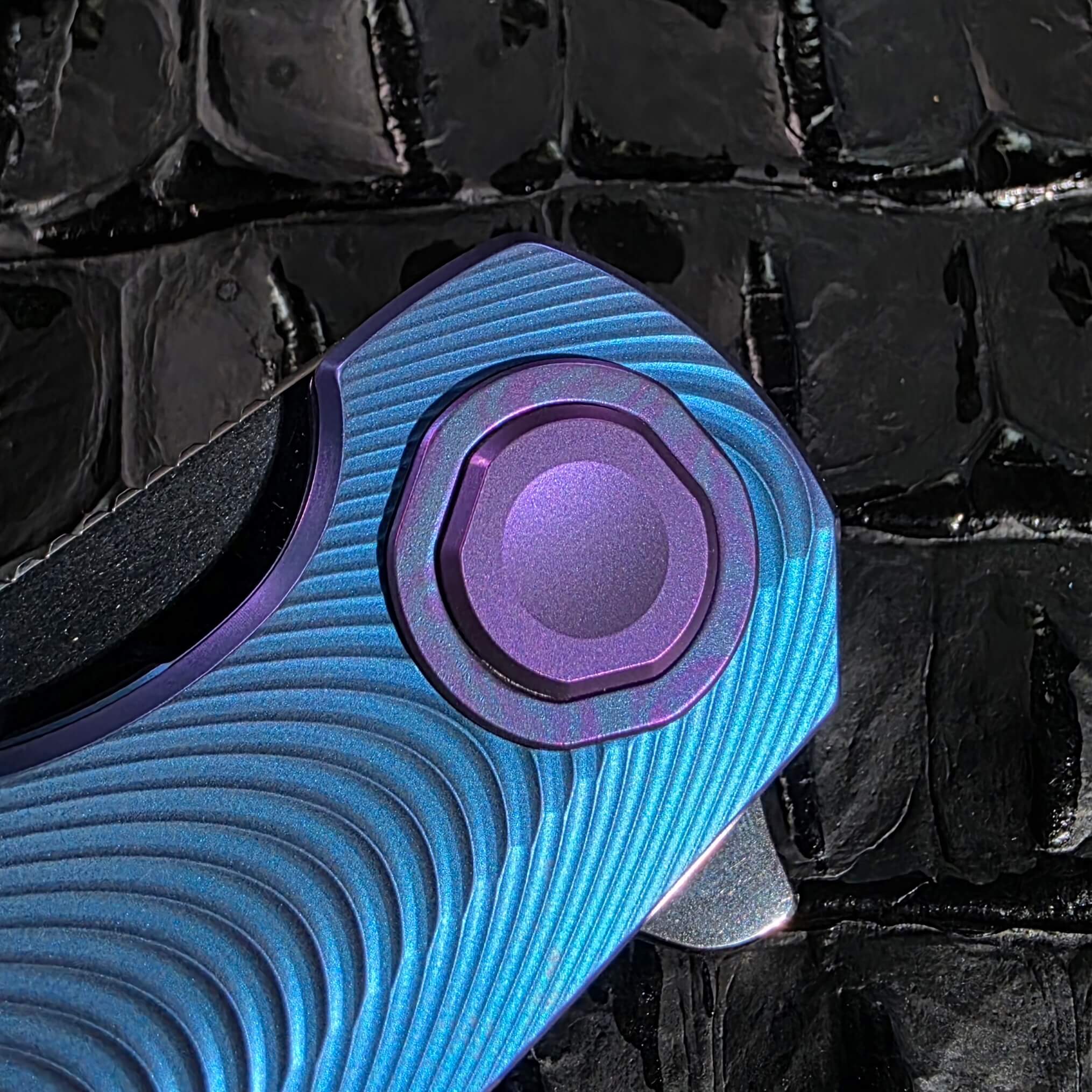 Macro of the heat-anodized Black Timascus pivot collar on the Holt Bladeworks Morpheus #1856 surrounded by Triad milling