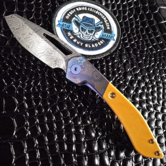Keanison Bloodhound liner lock #15 open show side beside the We Buy Knife Collections patch