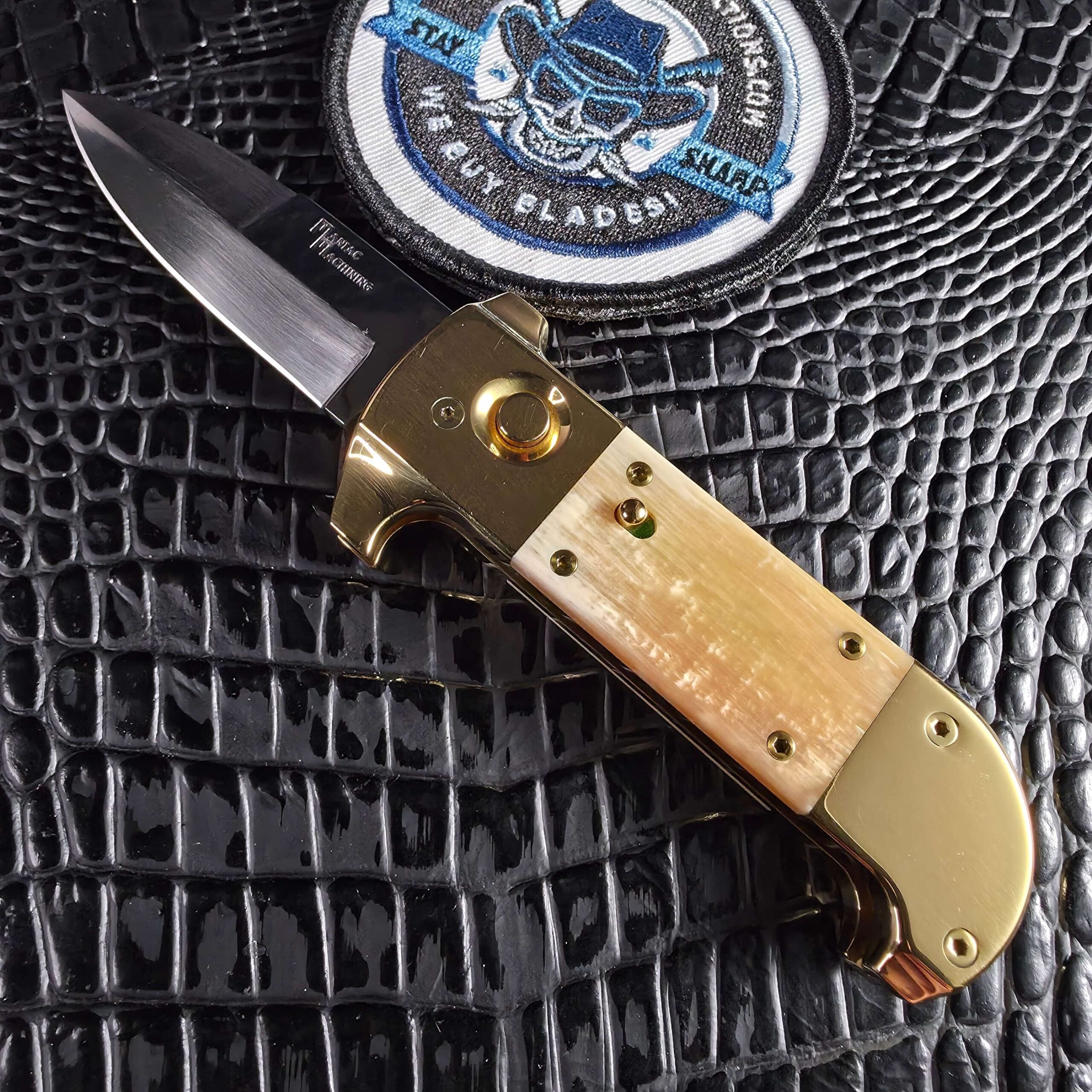 Maniac Machining Stinger Custom mammoth ivory automatic open beside the We Buy Knife Collections patch