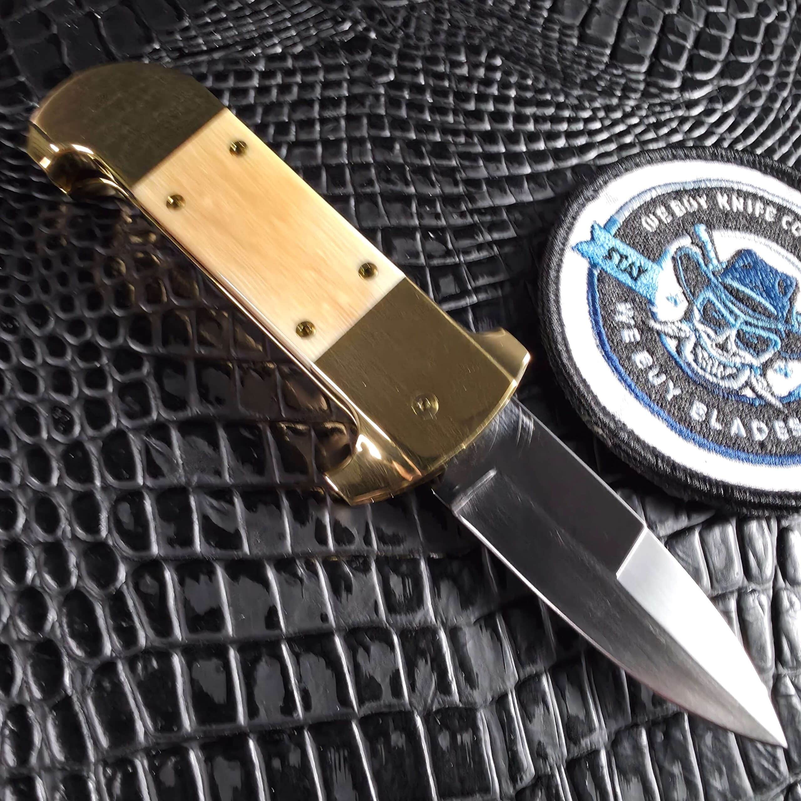 Reverse side of the Maniac Machining Stinger Custom automatic open beside the We Buy Knife Collections patch