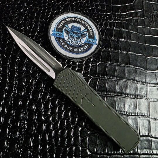 Medford Merc-1 OTF automatic dagger open beside the We Buy Knife Collections patch, 154CM blade and green aluminum handle