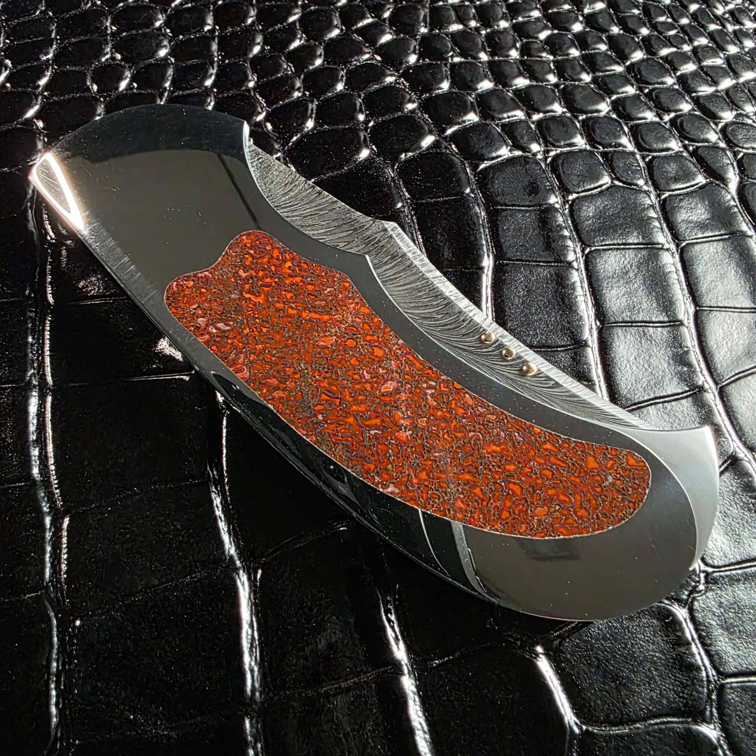 Detail of the feather damascus blade beside the red dinosaur bone inlay on the Scott Gallagher folder