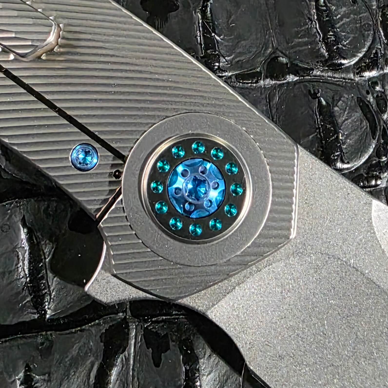 Macro of the seafoam anodized pivot collar on the Skiff Made Blades Fugitive #0113 showing thirteen teal micro screws around a blue center screw