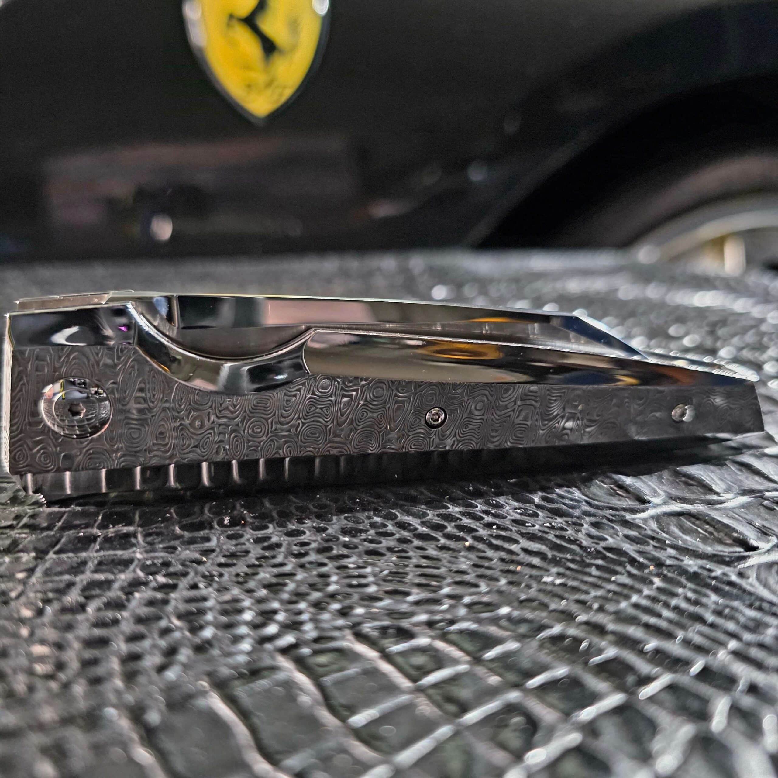 Low-angle side profile of the closed Stefano Compostella StriaXL showing the contoured spine, jimping, and Damasteel Ladder scale