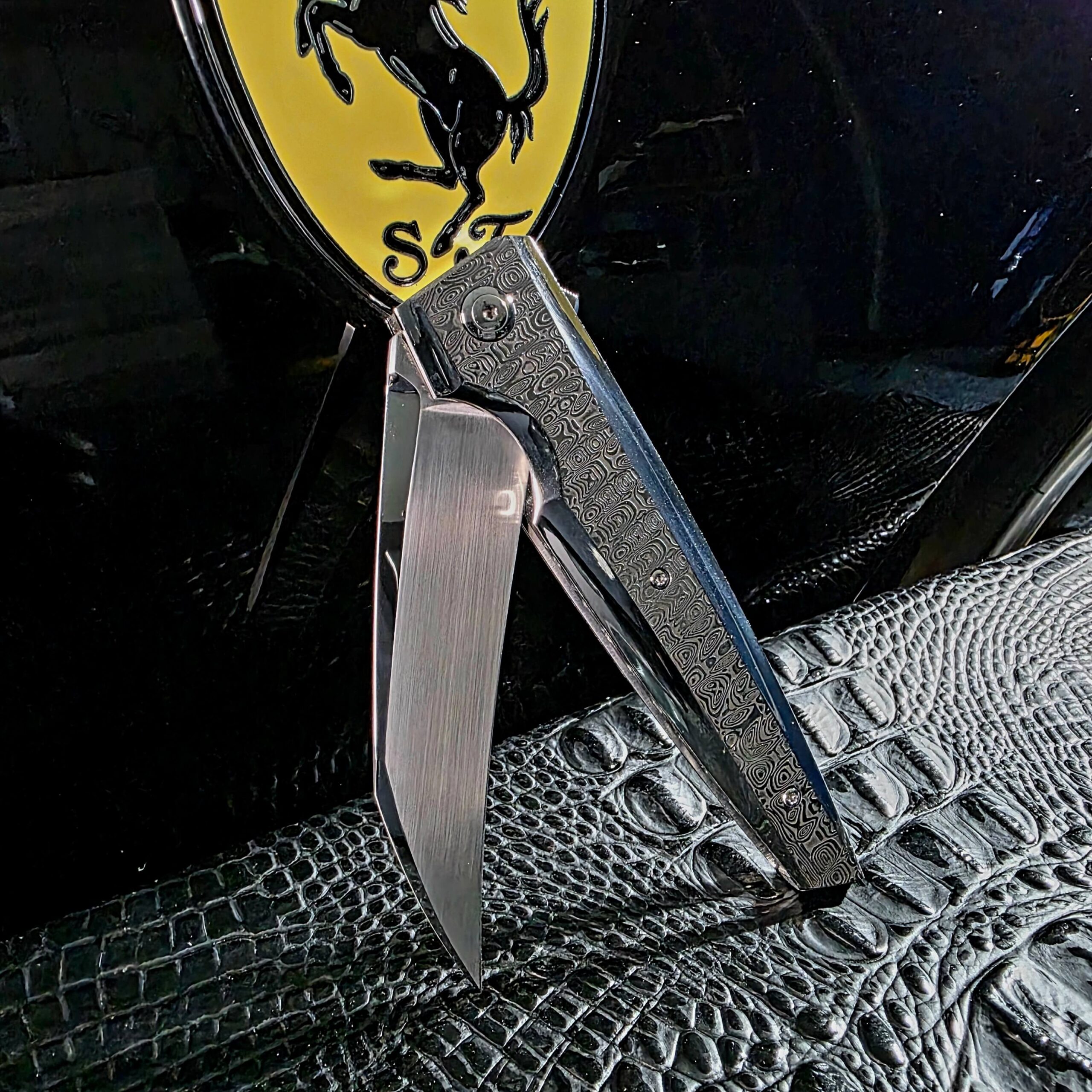 Stefano Compostella StriaXL custom flipper caught partially open, showing the Erasteel APZ10 blade swinging clear of the Damasteel Ladder handle