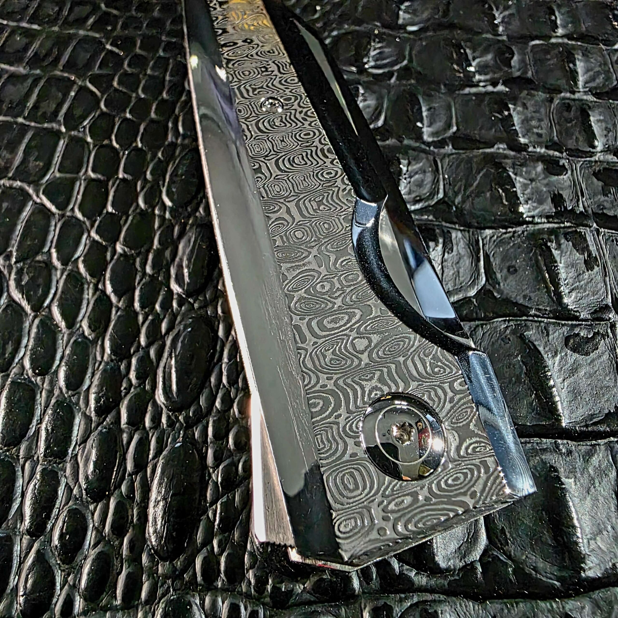 Close detail of the mirror-polished Damasteel Ladder scale, flipper tab, and polished stainless pivot on the Stefano Compostella StriaXL