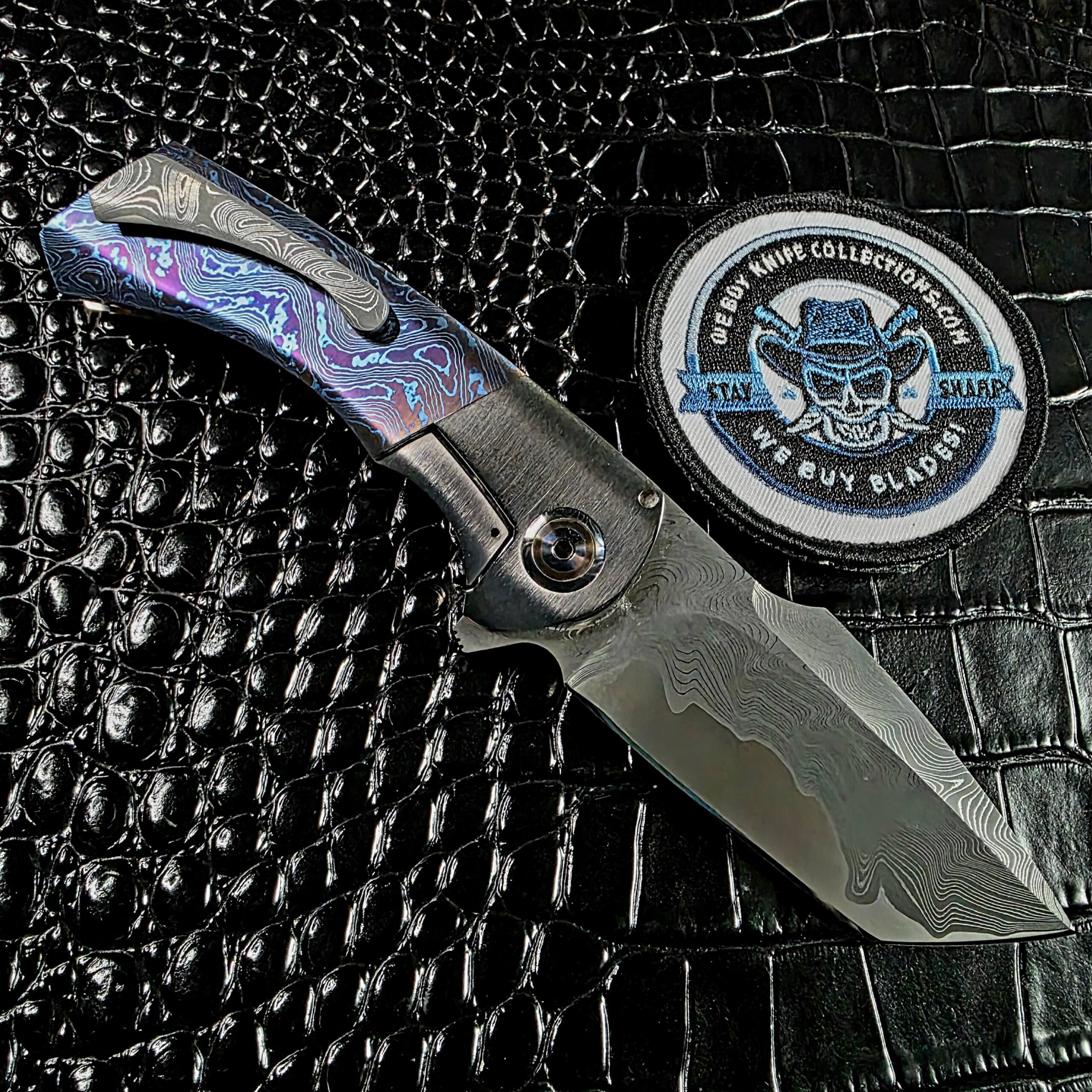 Todd Fischer Kamehameha open on the clip side beside the We Buy Knife Collections patch, San Mai damascus pocket clip
