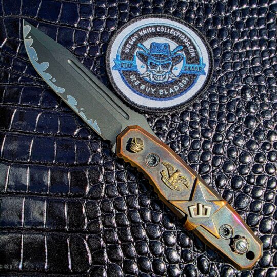 Blackside Customs Plan B on the show side, CPM MagnaCut blade with Suminagashi wave above hand-carved copper scales by Starlingear, with the We Buy Knife Collections patch in frame