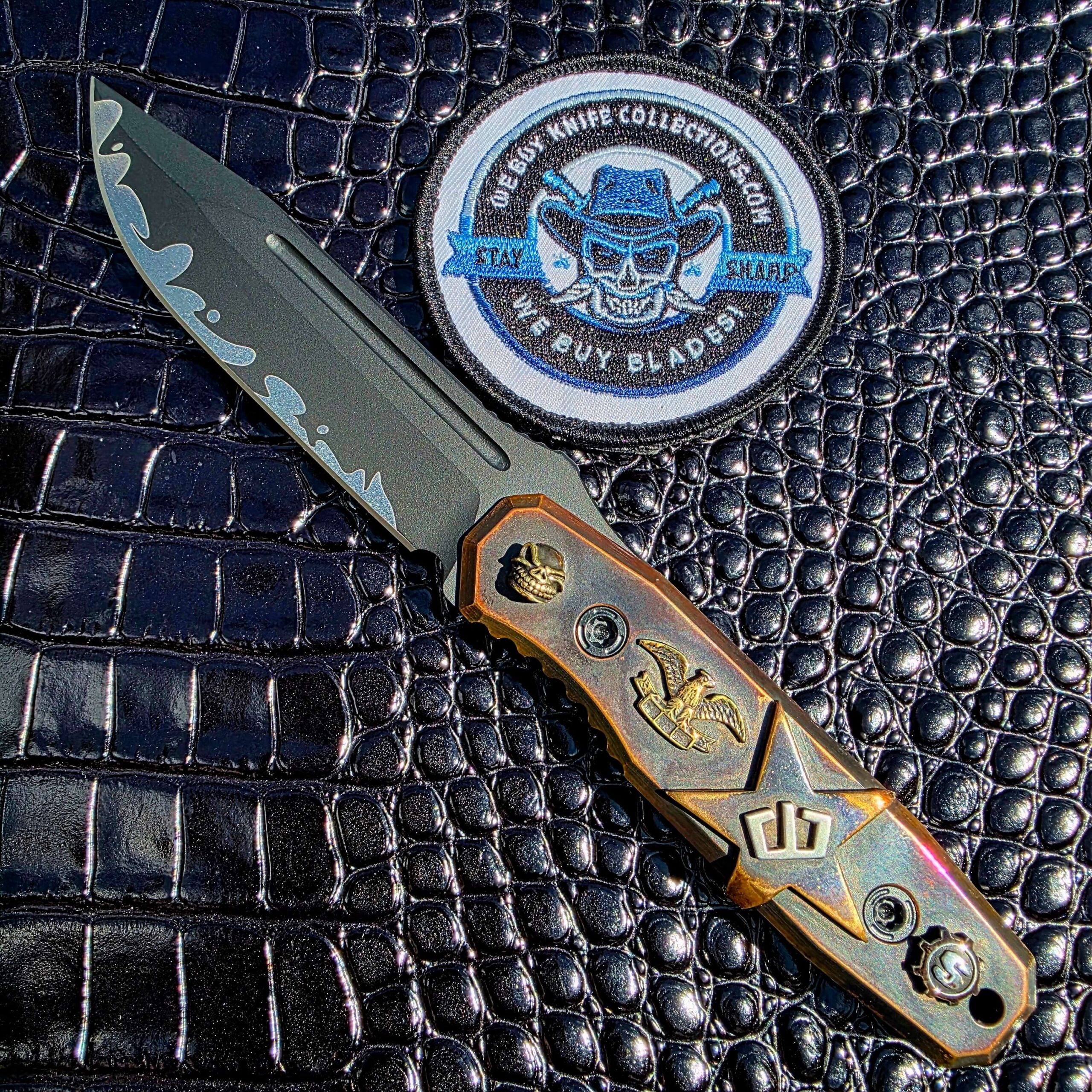 Blackside Customs Plan B on the show side, CPM MagnaCut blade with Suminagashi wave above hand-carved copper scales by Starlingear, with the We Buy Knife Collections patch in frame