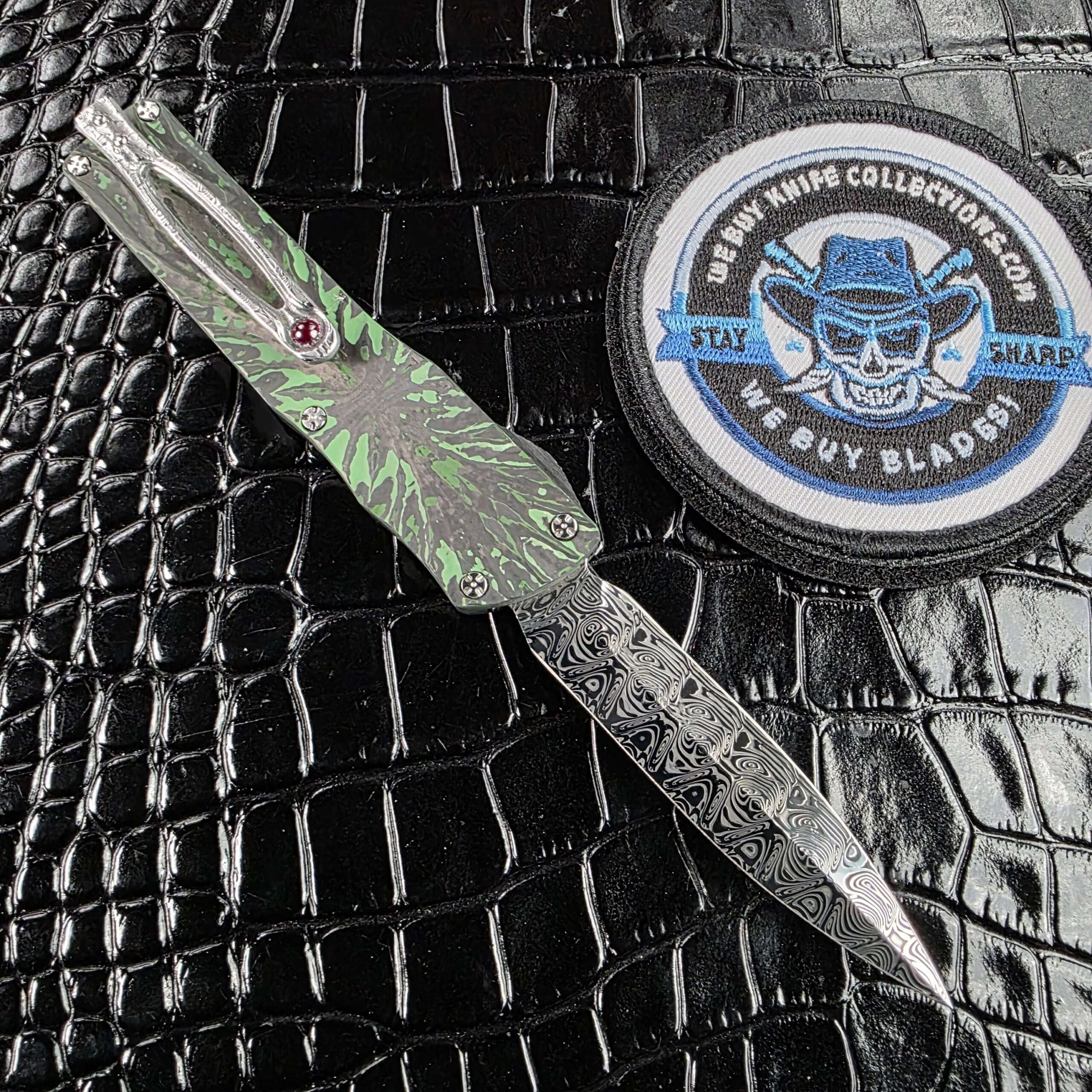 Brian Tighe Tighe Twist OTF deployed on the clip side, showing the green carbon fiber face and Damasteel pocket clip with ruby ball