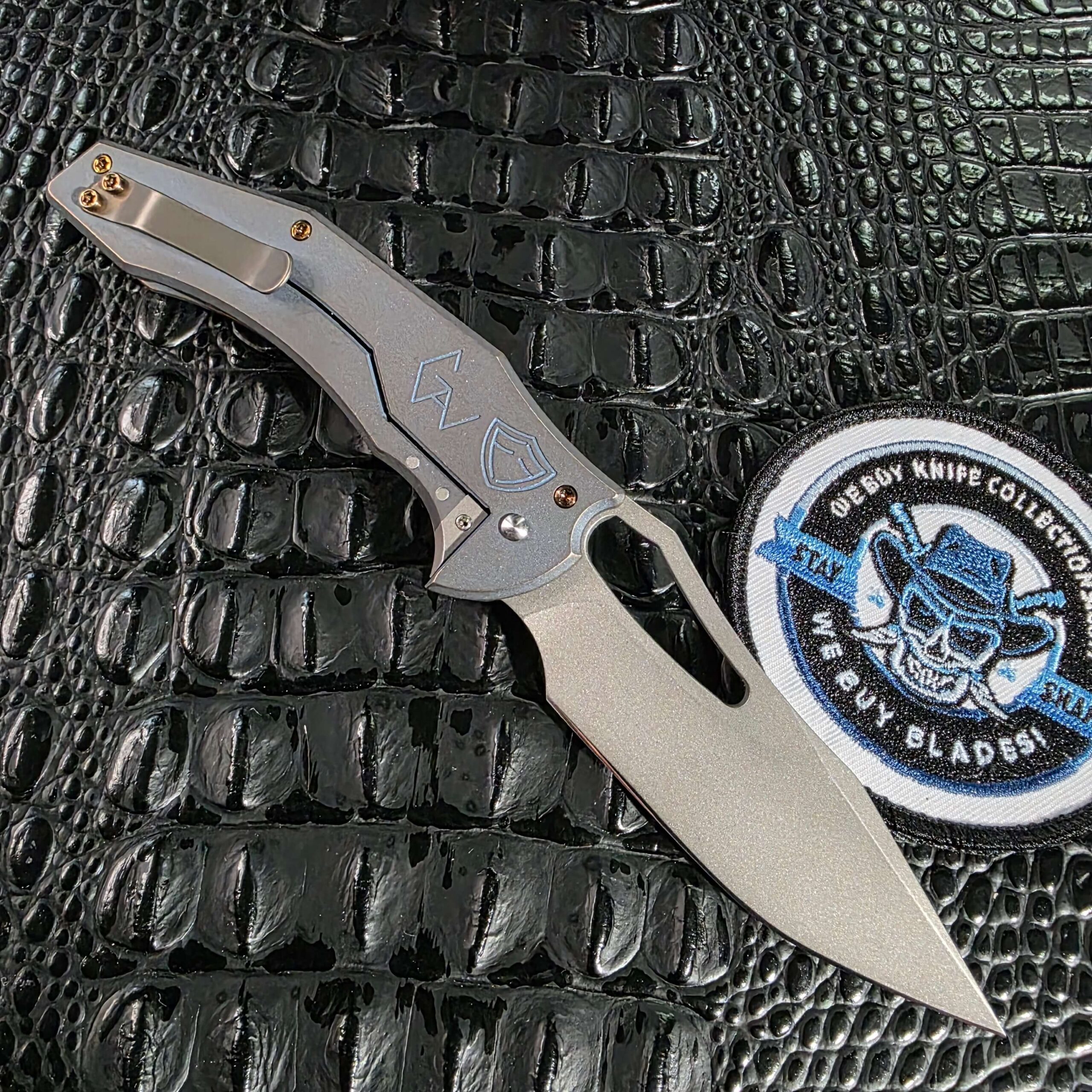 Ferrum Forge x Gavko Spinner open on the clip side showing the sculpted titanium pocket clip and frame lock, with the We Buy Knife Collections patch in frame