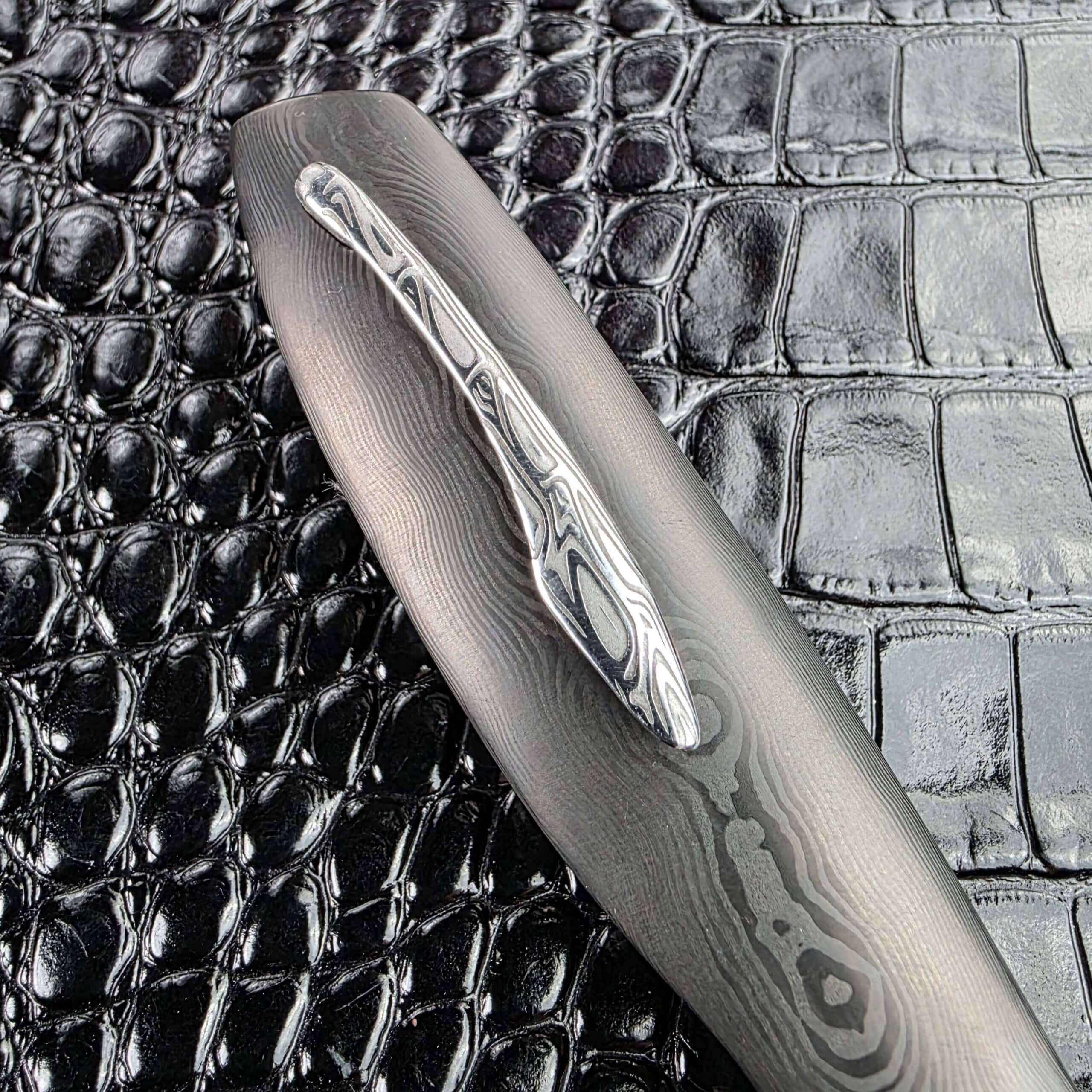 Sculpted Damasteel Svavner pocket clip on the Glenn Are Hovin Koda, set into the layered carbon fiber scale