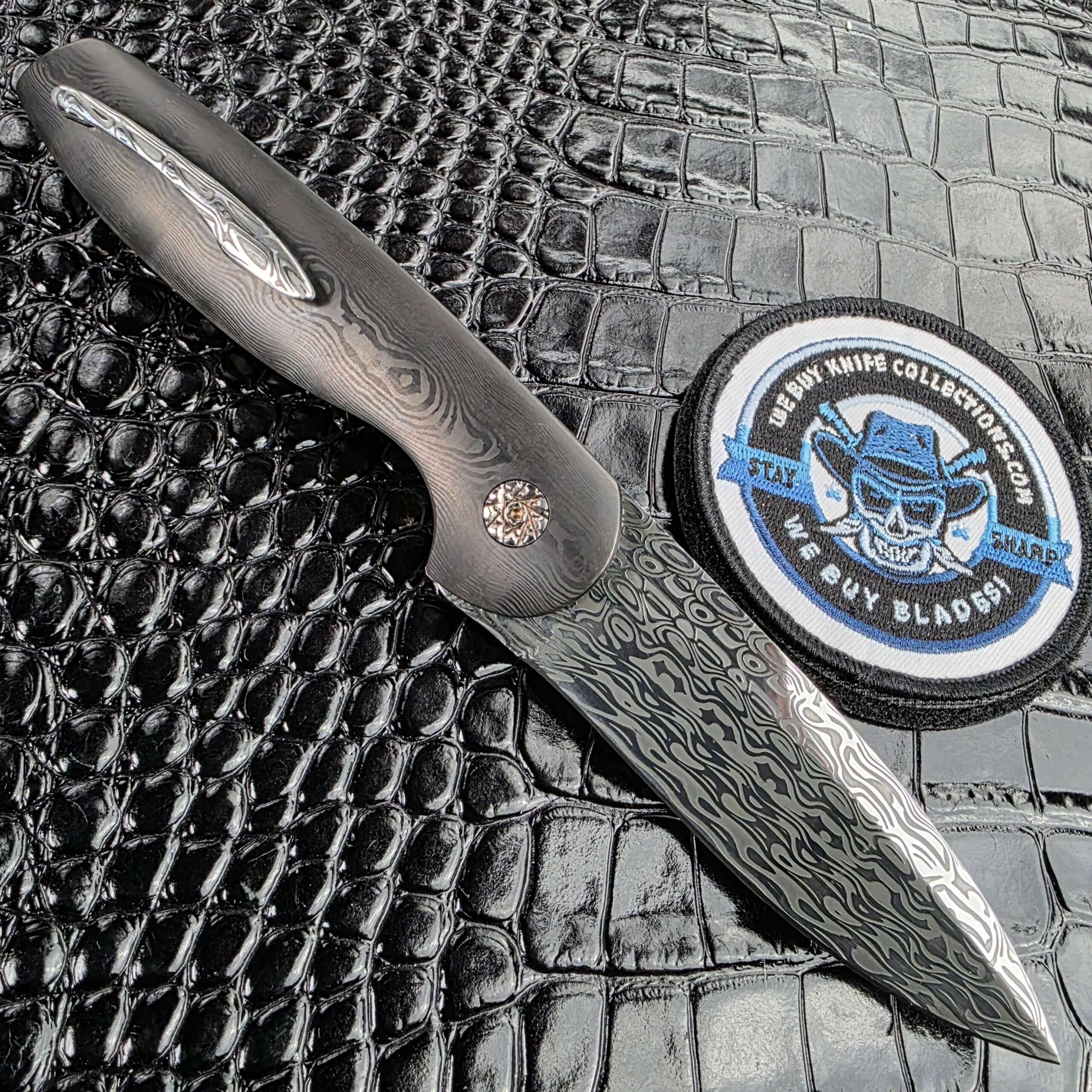 Glenn Are Hovin Koda open on the clip side with the Damasteel pocket clip visible and the We Buy Knife Collections patch in frame