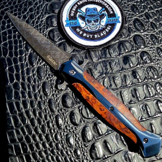 La Cantina Sally #453 open on the show side, Gianluca Spina mosaic damascus dagger blade above a DLC steel frame with ironwood inlay, with the We Buy Knife Collections patch in frame