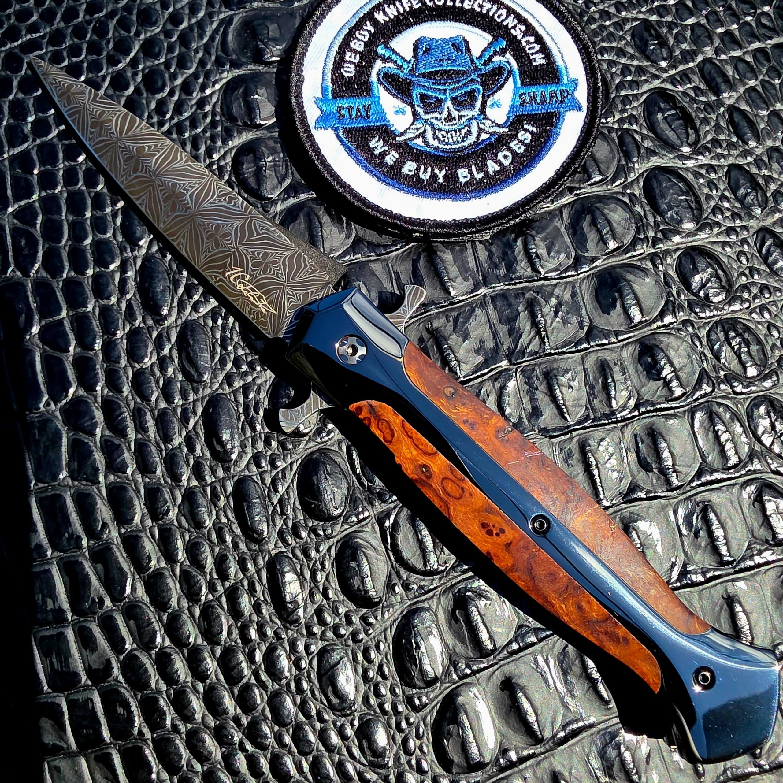 La Cantina Sally #453 open on the show side, Gianluca Spina mosaic damascus dagger blade above a DLC steel frame with ironwood inlay, with the We Buy Knife Collections patch in frame