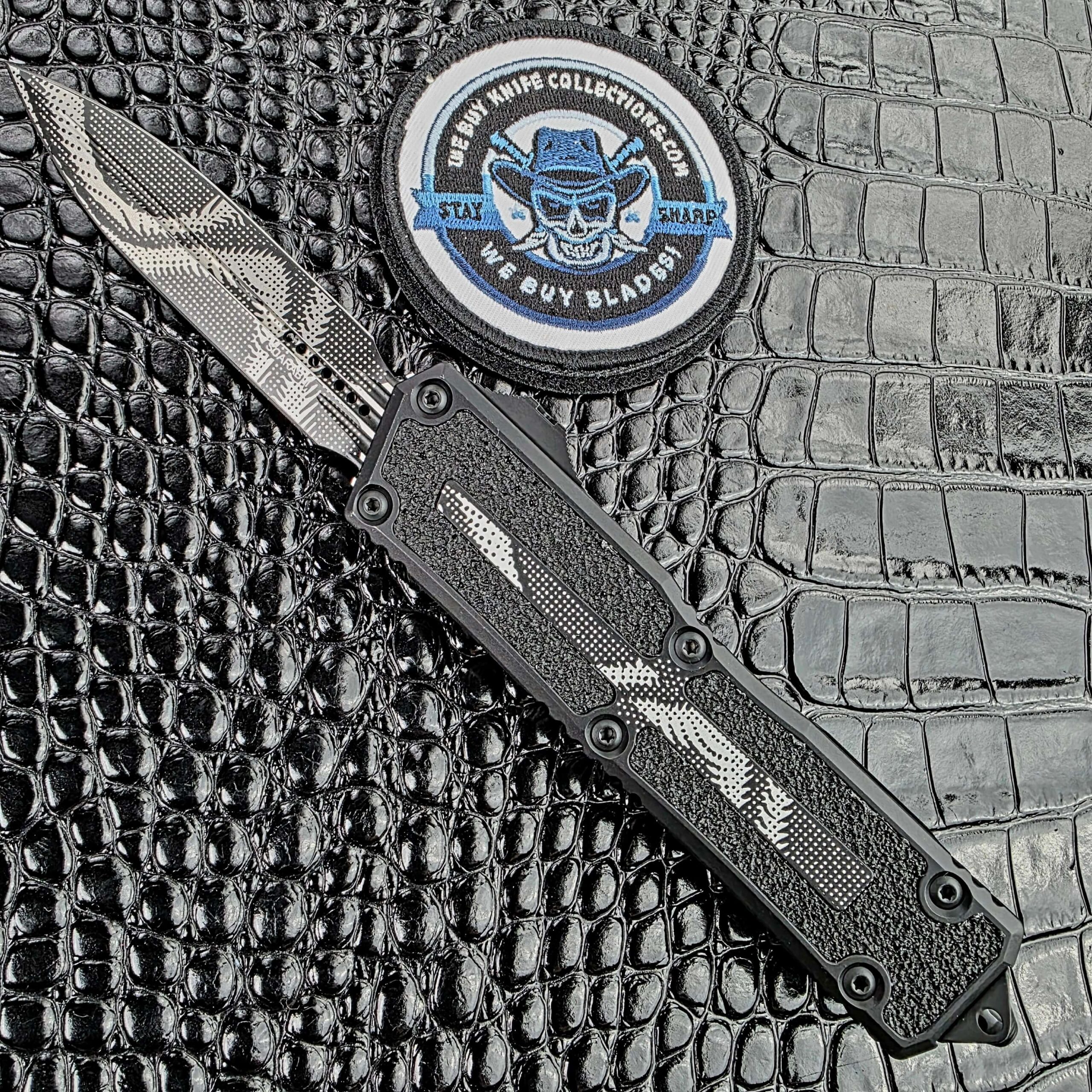 Microtech Scarab II Gen III deployed on the show side, Geo Trace Camo D/E dagger blade and aluminium handle with 3M grip inserts, with the We Buy Knife Collections patch in frame
