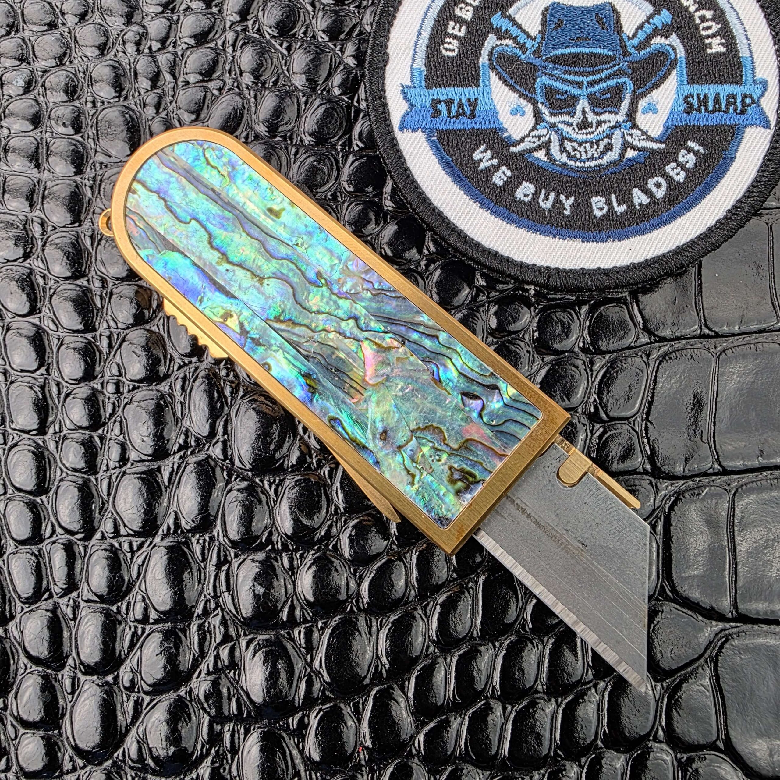 Miroc Razor Knife OTF Automatic Custom from the reverse with the blade deployed, showing the full abalone scale, with the We Buy Knife Collections patch in frame