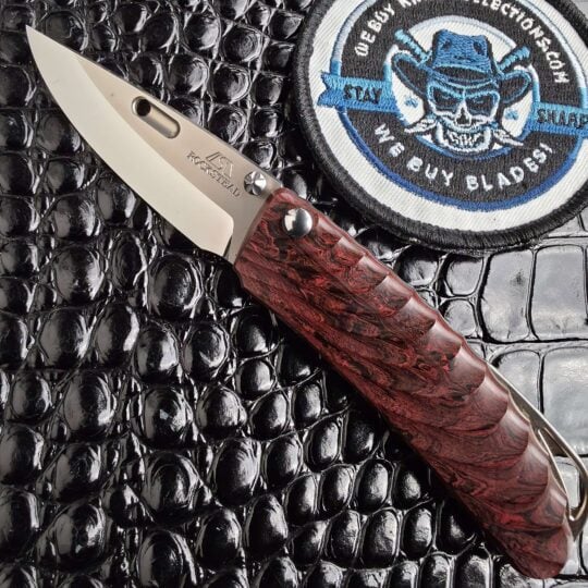 Rockstead NEHAN open with mirror-polished ZDP-189 blade and milled ebonite scales, with the We Buy Knife Collections patch in frame