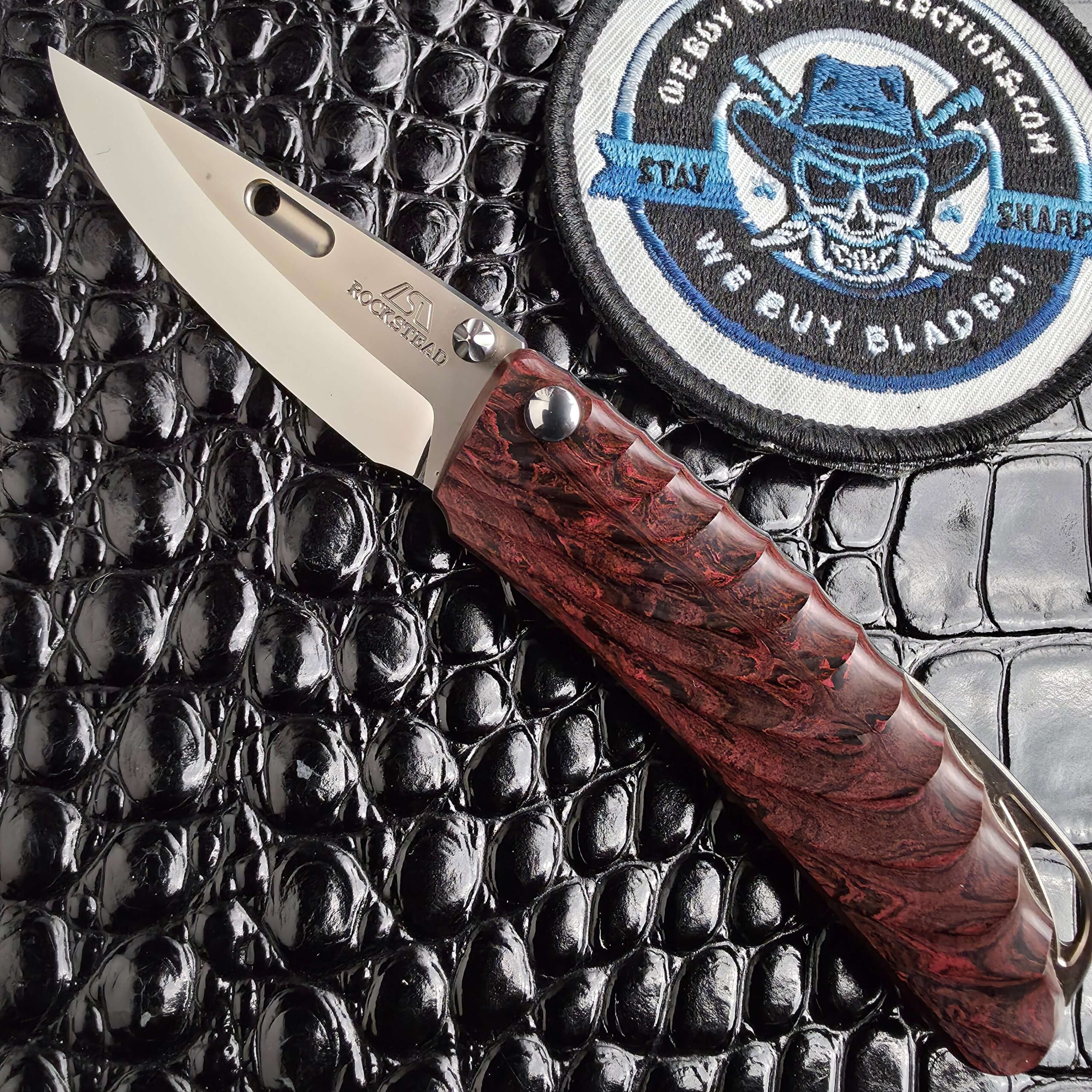 Rockstead NEHAN open with mirror-polished ZDP-189 blade and milled ebonite scales, with the We Buy Knife Collections patch in frame