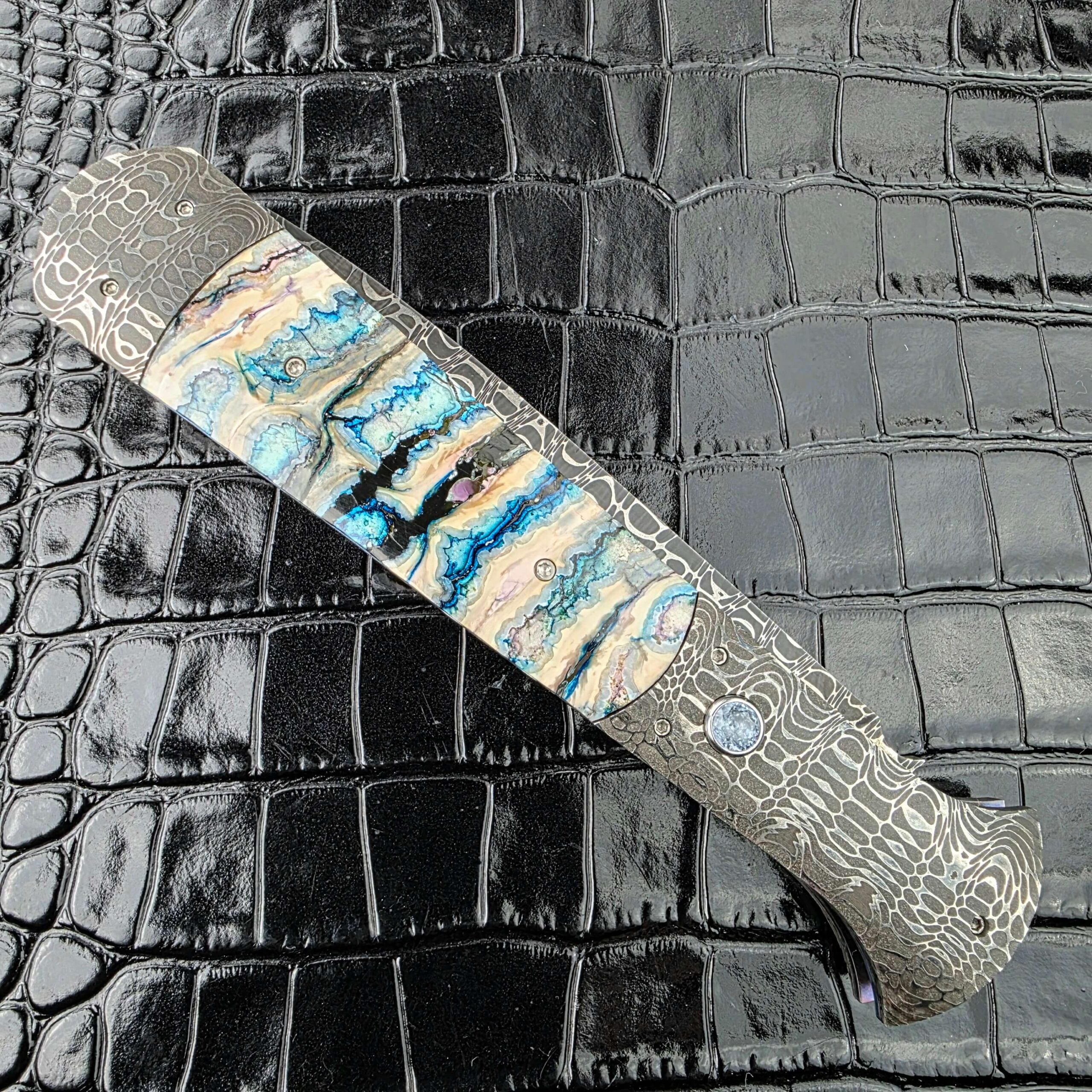 Burn Knives Automatic Dagger closed on the show side with mammoth molar between Damascus bolsters
