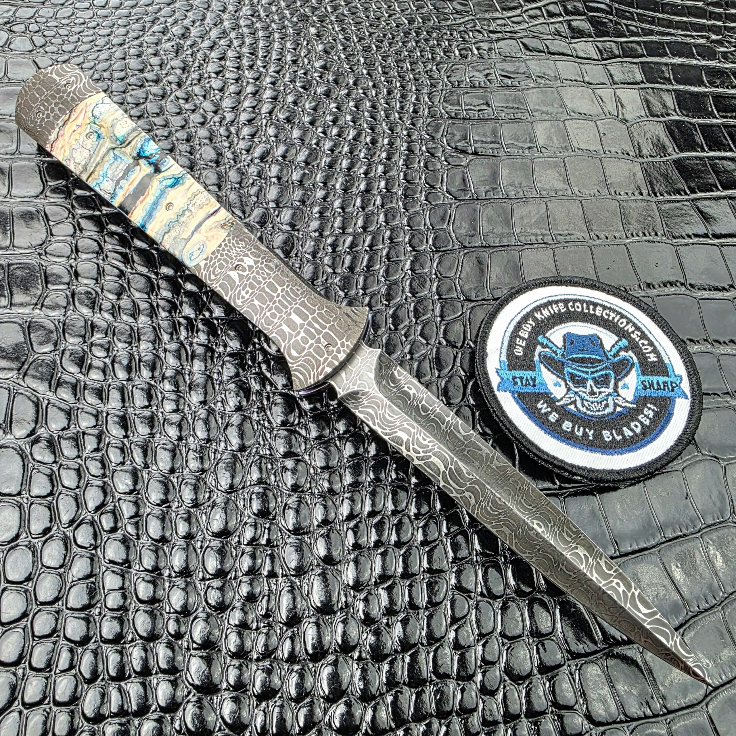 Burn Knives Automatic Dagger open on the lock side showing the symmetrical dagger grind, with the We Buy Knife Collections patch in frame