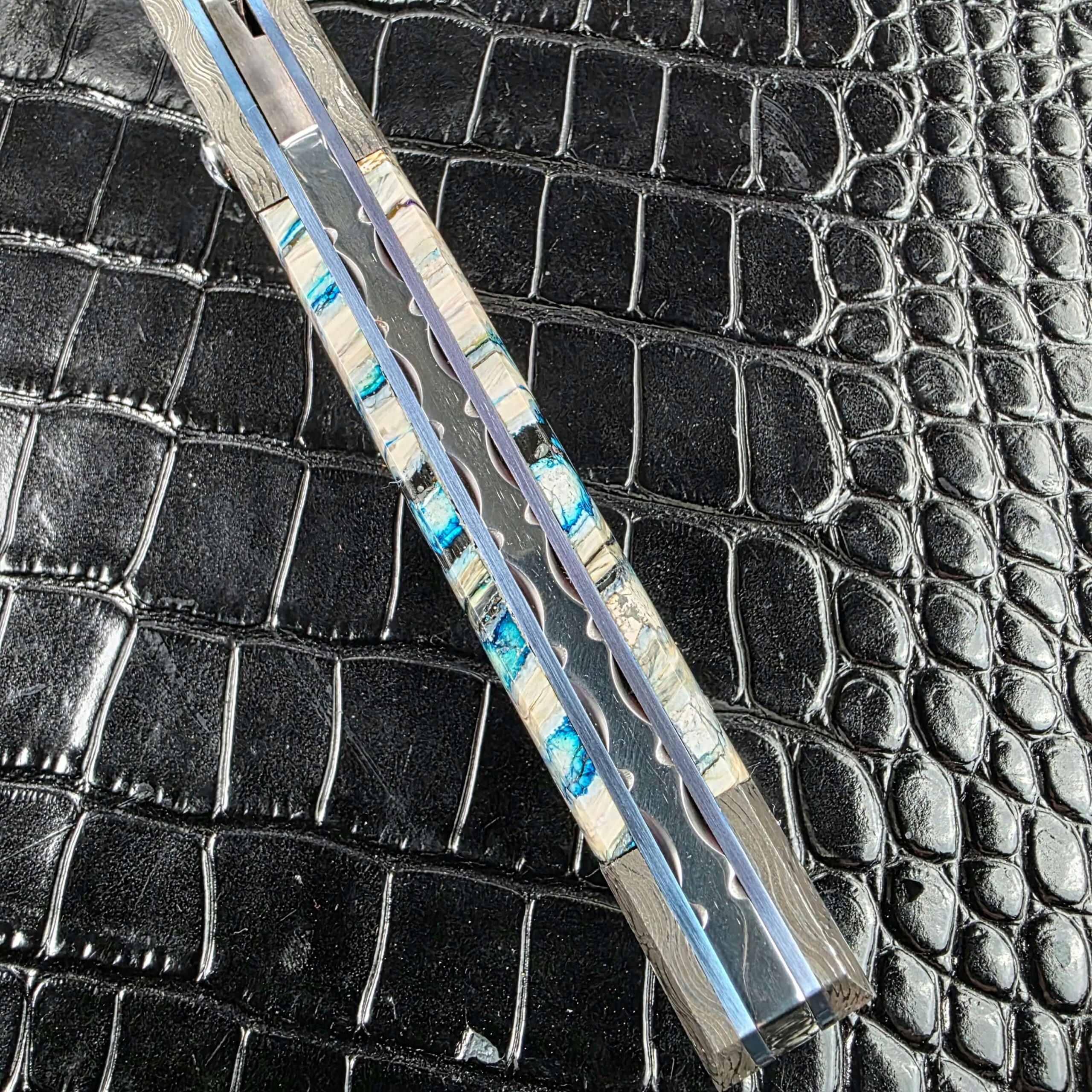 Blue anodized titanium liners with a milled wave along the spine of the Burn Knives Automatic Dagger