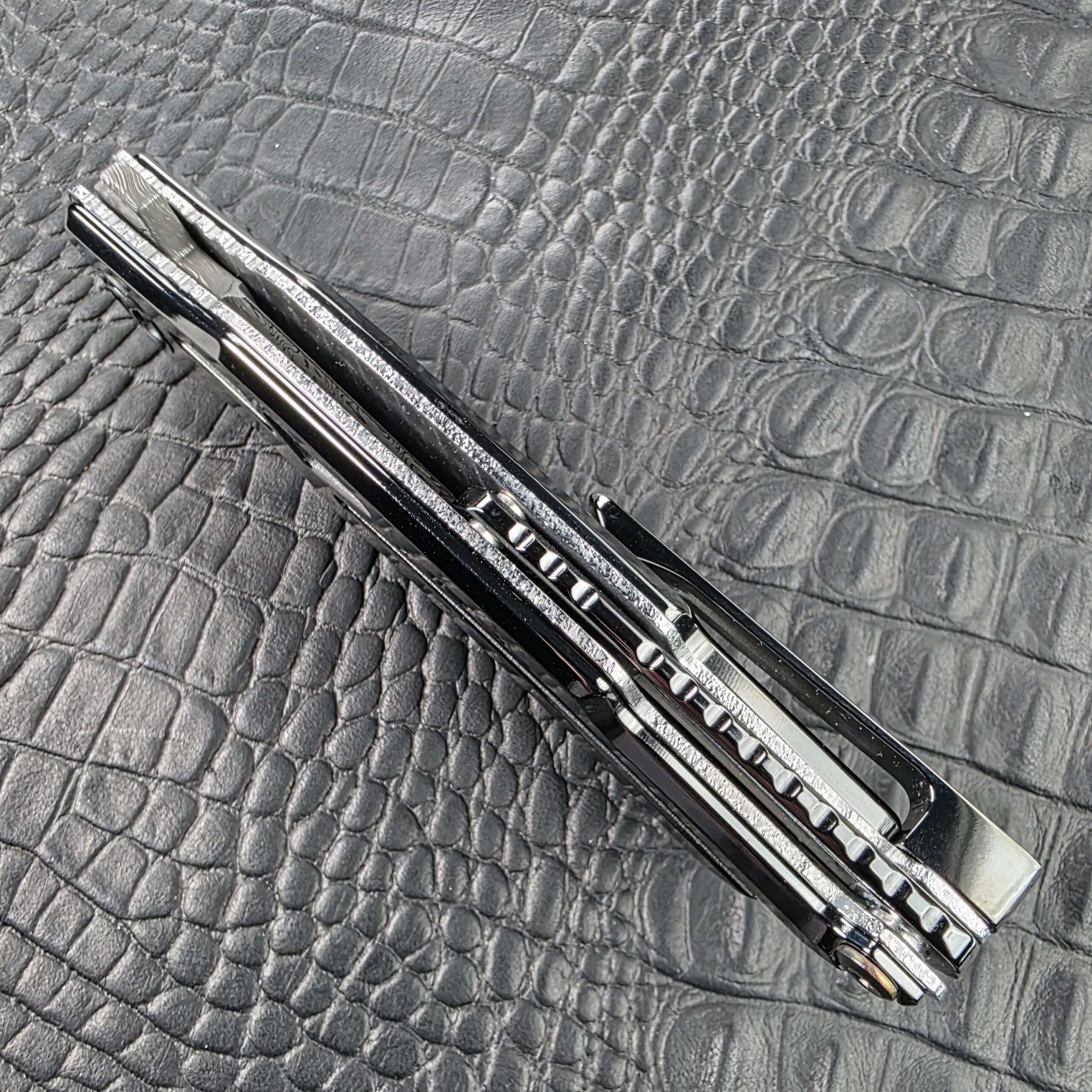 Spine view of the closed Dew Hara Seismic Damascus Ray showing the notched DLC Titanium backbar and the pocket clip