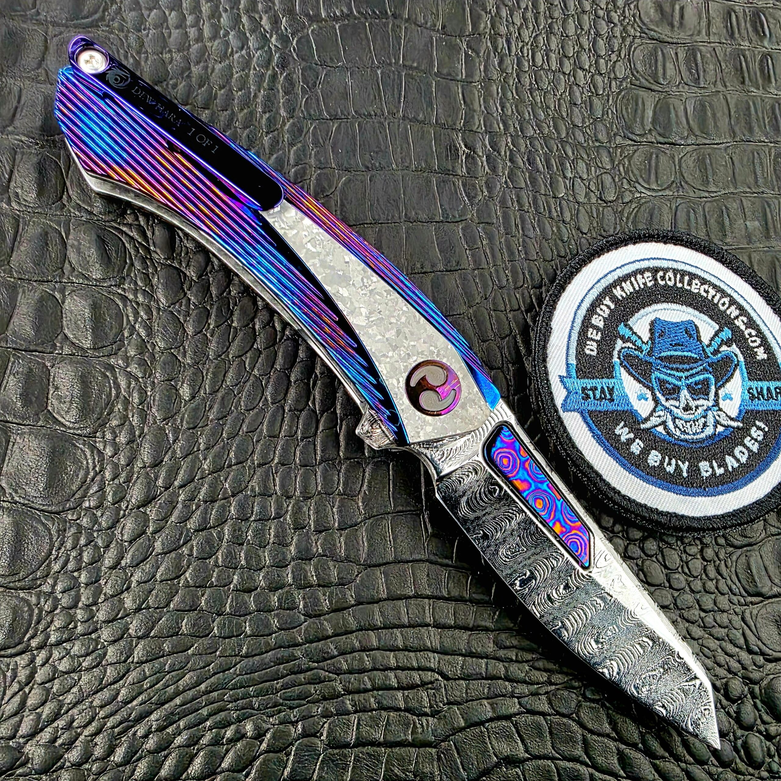 Dew Hara Sharktooth Damascus METEOR open on its clip side with the Titanium pocket clip and the We Buy Knife Collections patch