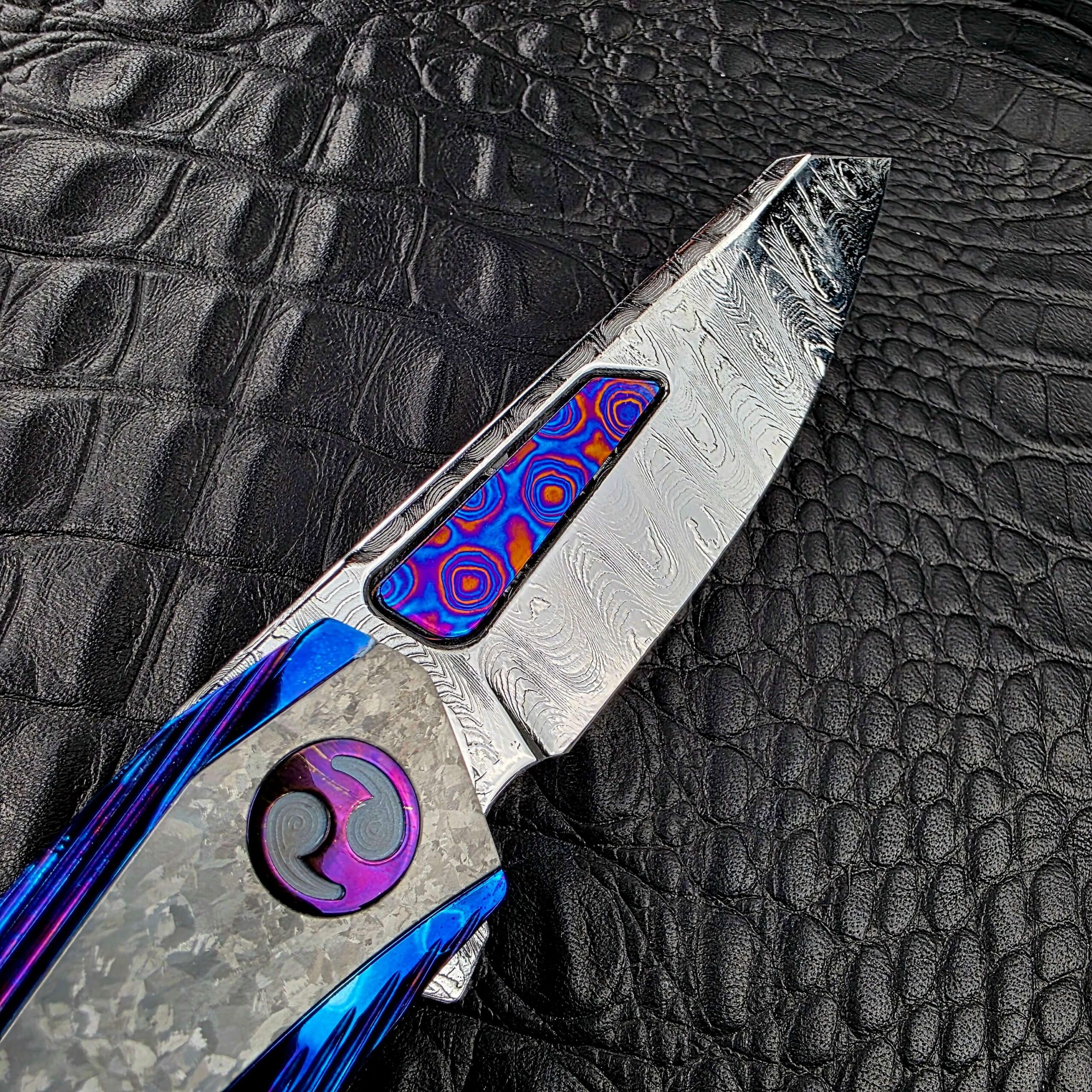Titanium pocket clip on the Dew Hara METEOR marked with the Dew Hara logo and DEW HARA 1 OF 1, over grooved Timascus