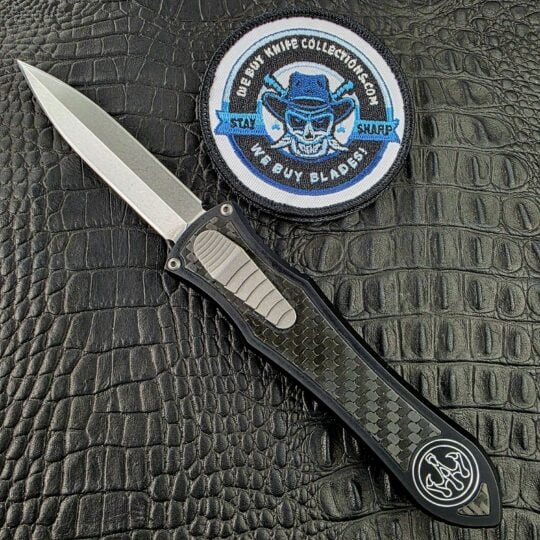 Hawk Deadlock Model C open on its show side with a CPM 20CV double-edge dagger and woven Carbon Fiber inlay beside the We Buy Knife Collections patch