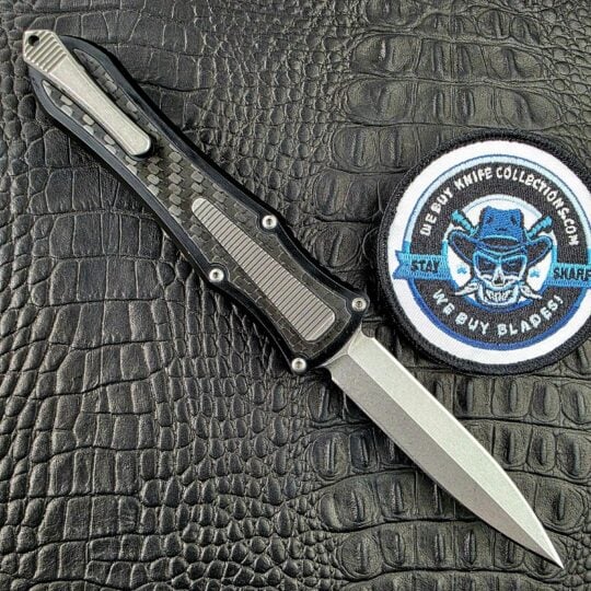 Hawk Deadlock Model C open on its clip side, with the Titanium pocket clip, fluted panel and Carbon Fiber inlay, beside the We Buy Knife Collections patch