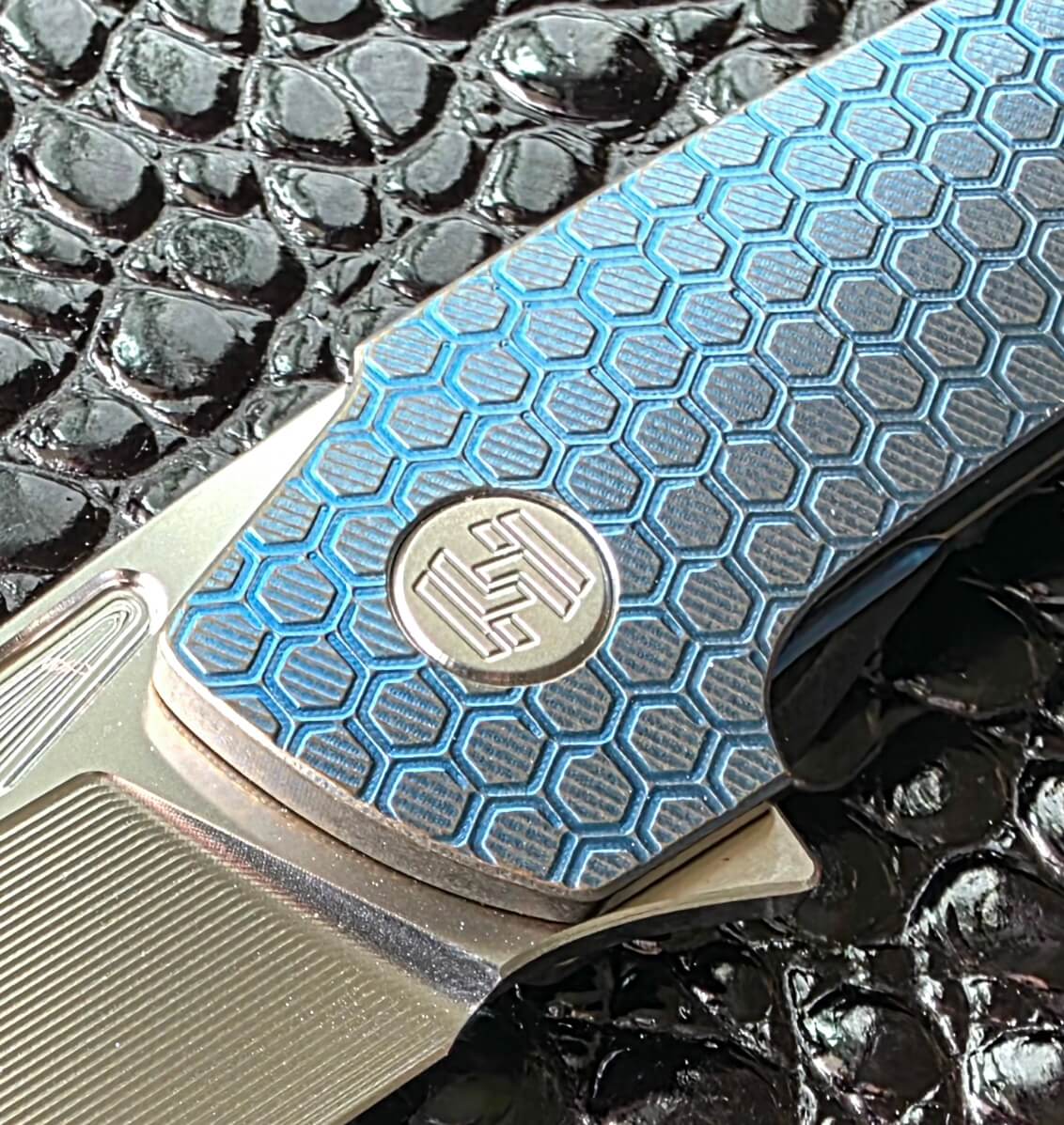 Macro of the Hog House honeycomb milling and the engraved Hog House emblem pivot collar in blue anodized titanium