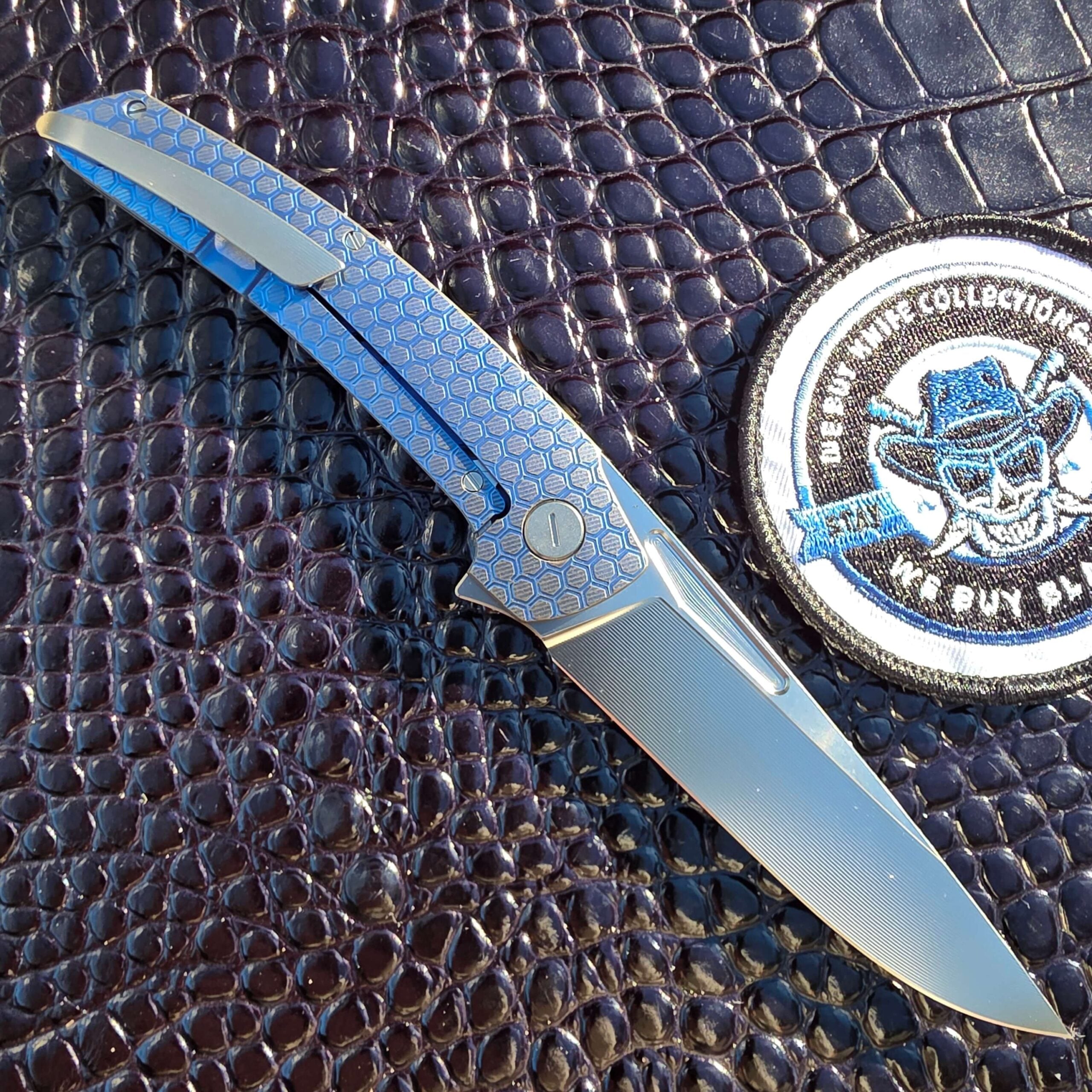 Hog House Honeycomb Model T Gen 2 open on the clip side showing the 3D-milled titanium pocket clip, We Buy Knife Collections patch in frame