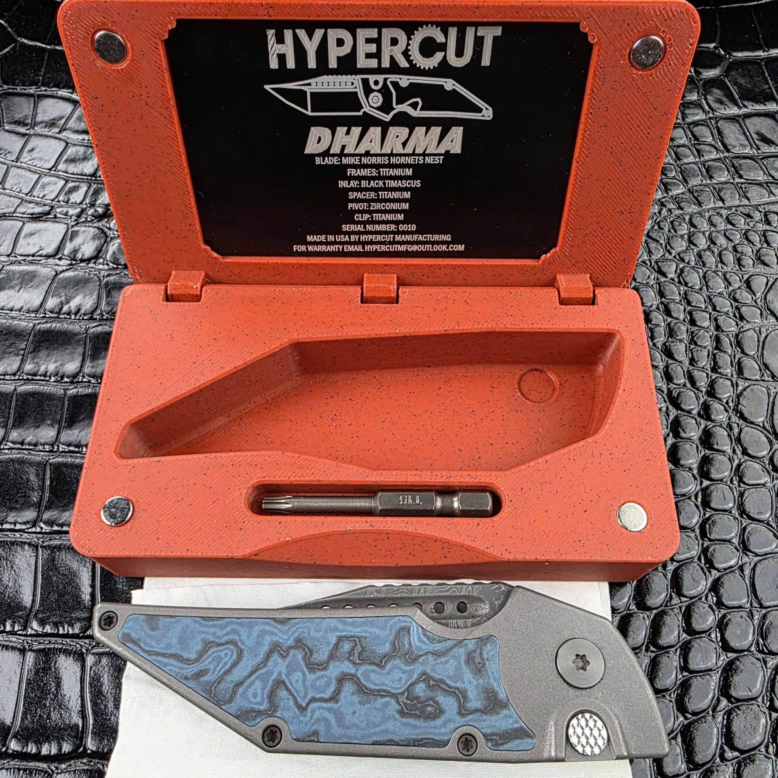 Hypercut Dharma on its cleaning cloth below its open 3D-printed case, with the COA plate in the lid and a T15 bit in the base