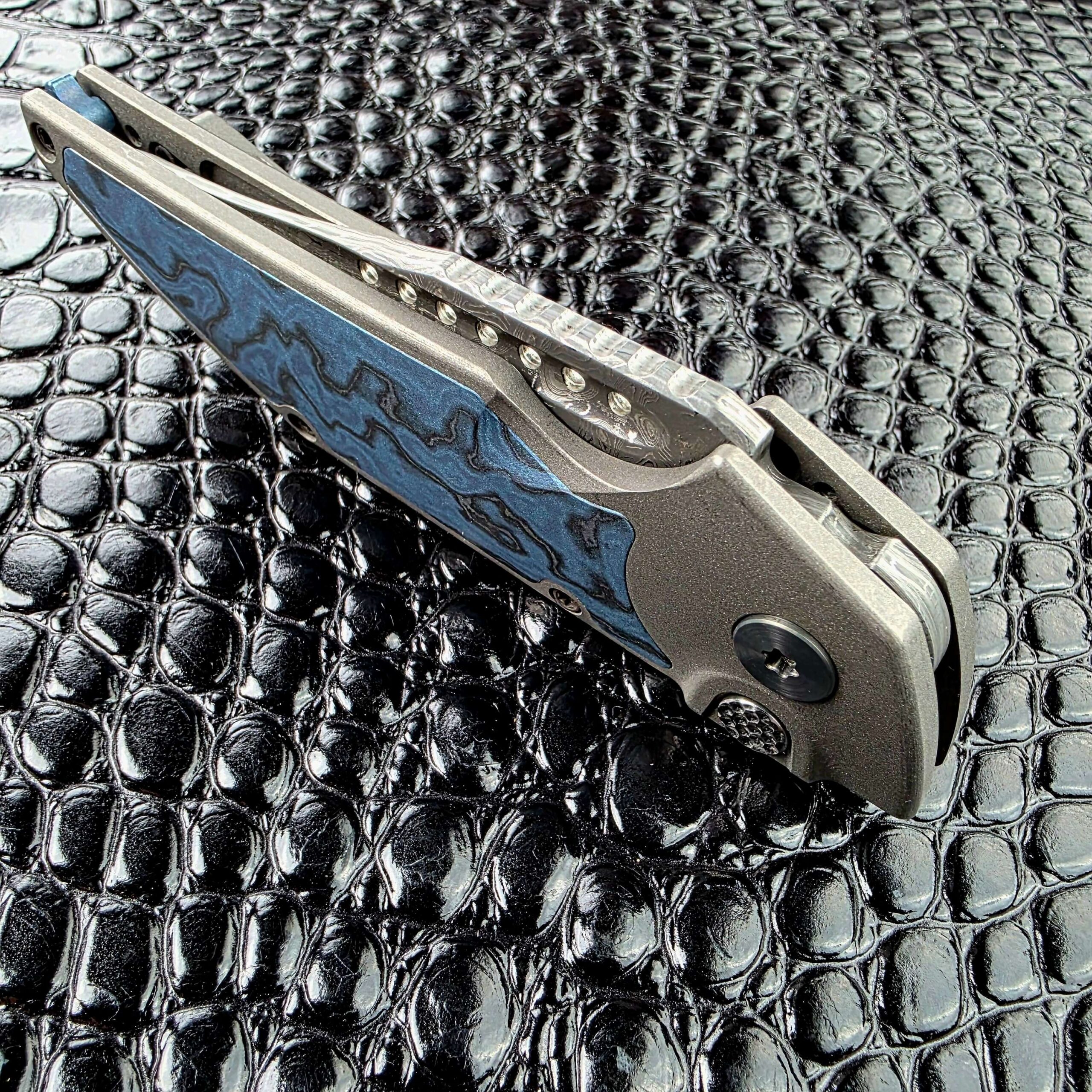 Angled view of the Hypercut Dharma’s jimped Damascus blade spine and fuller holes above the Titanium frame
