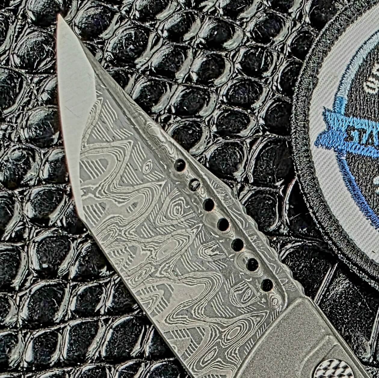 Close view of the Mike Norris Hornets Nest Damascus tanto on the Hypercut Dharma, with its fuller holes and jimped spine