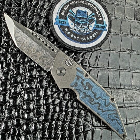 Hypercut Dharma open on its show side with a Mike Norris Hornets Nest Damascus tanto beside the We Buy Knife Collections patch