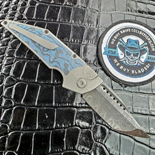 Hypercut Dharma open on its clip side with the milled Titanium clip over the Black Timascus inlay beside the We Buy Knife Collections patch