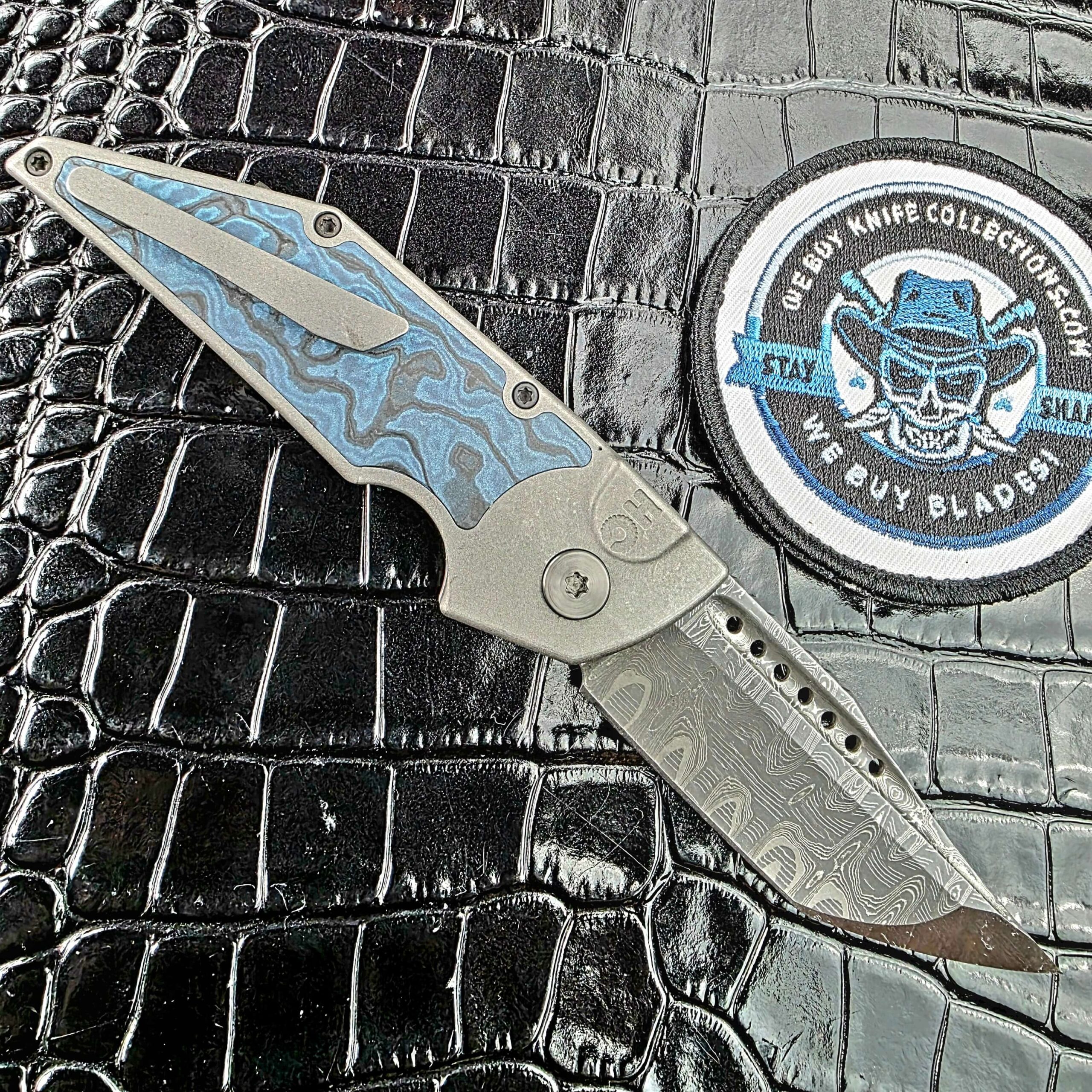 Hypercut Dharma open on its clip side with the milled Titanium clip over the Black Timascus inlay beside the We Buy Knife Collections patch