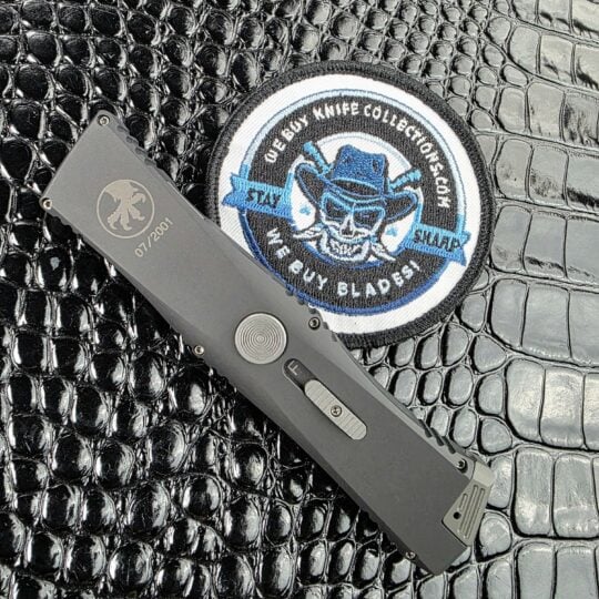 Closed Microtech Exodus on its show side beside the We Buy Knife Collections patch