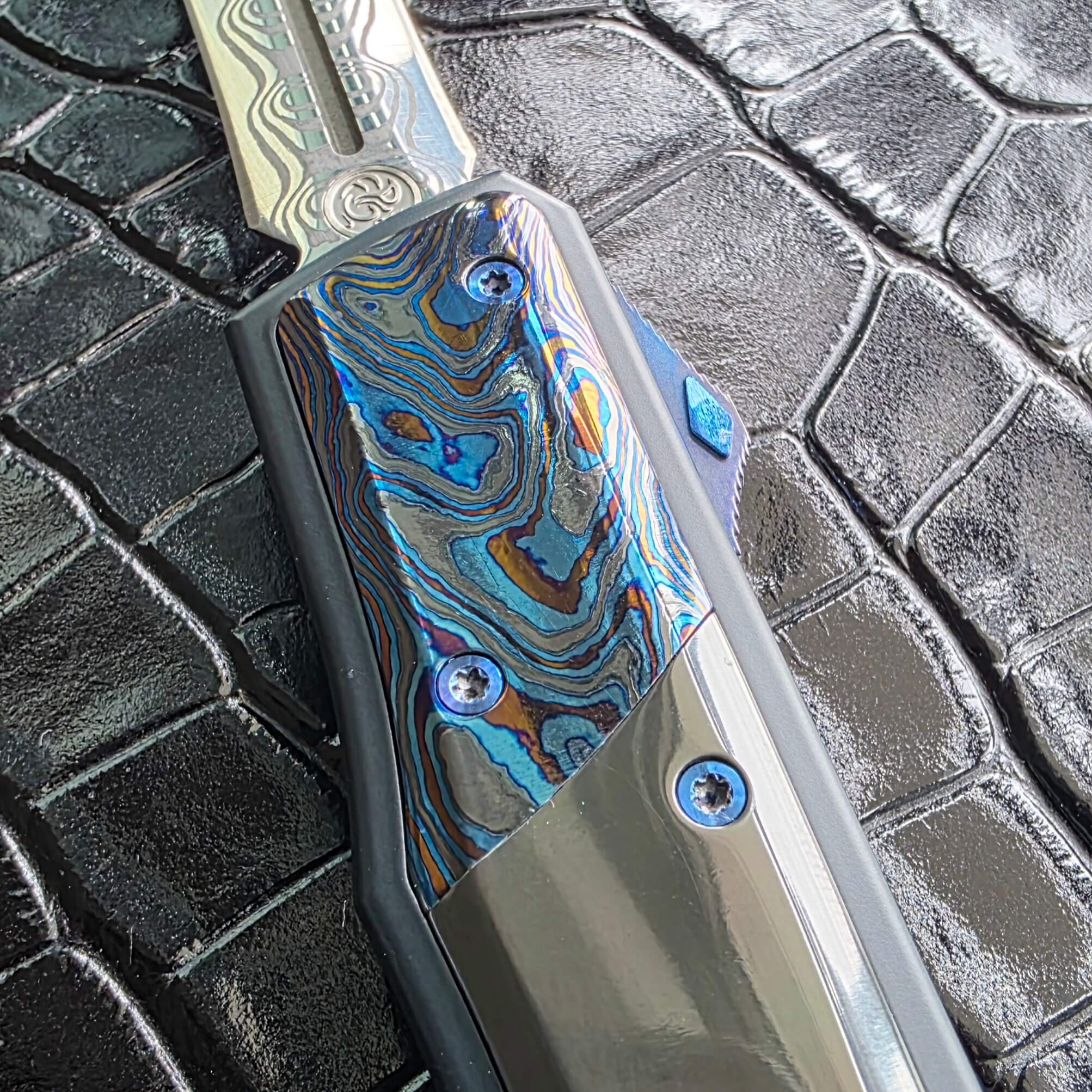 Macro of the Black Timascus bolster on the Patrick Famin GOTF Mini with blue anodized hardware