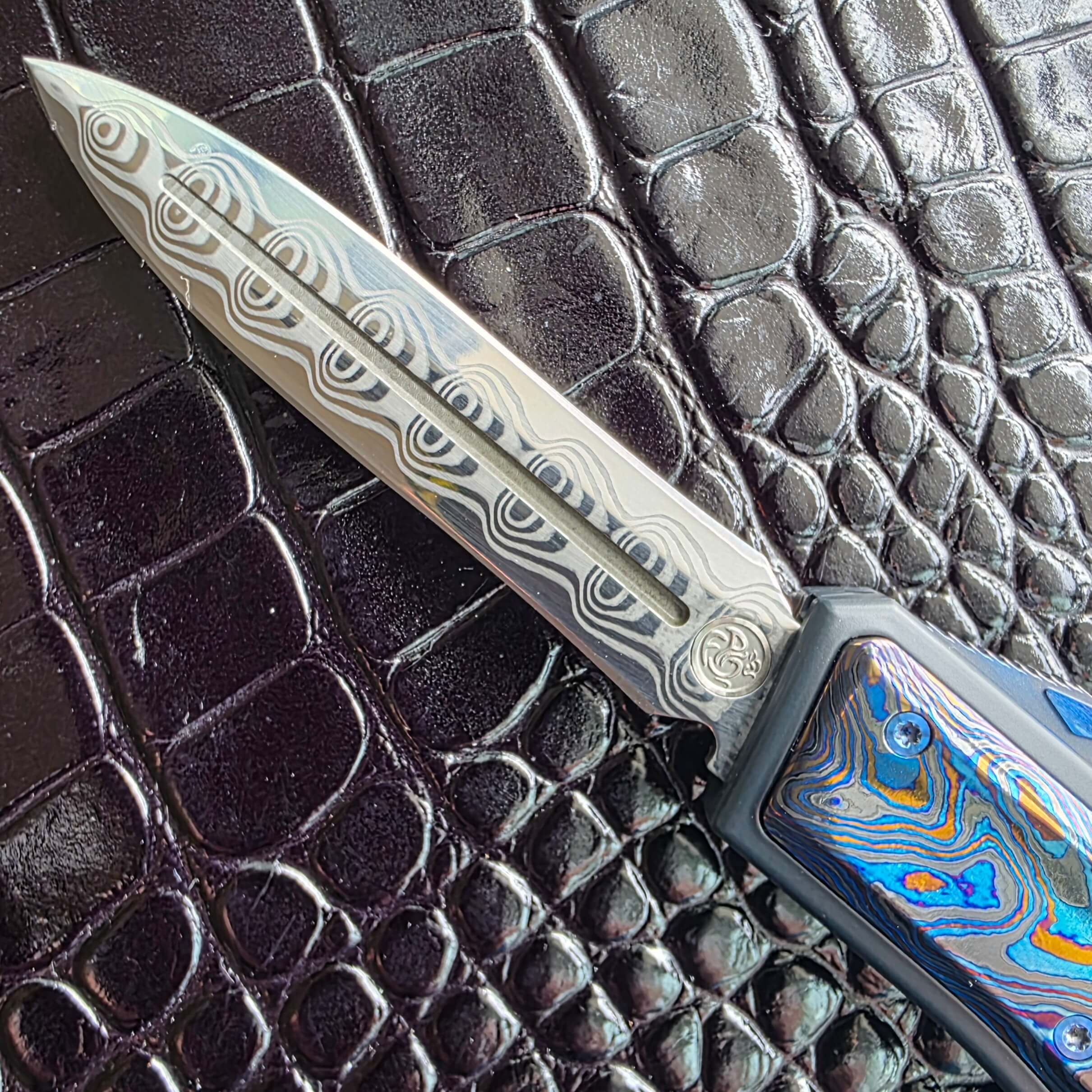 Macro of the Damasteel Damacore dagger blade on the Patrick Famin GOTF Mini showing the concentric wave pattern and fuller