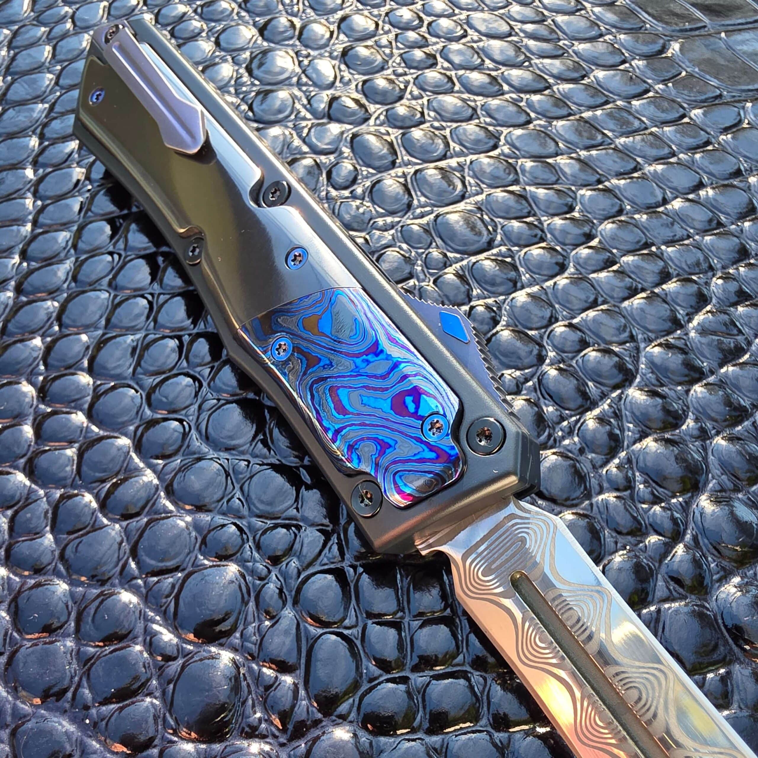 Patrick Famin GOTF Mini open on the clip side under cool lighting, Black Timascus reading blue and magenta